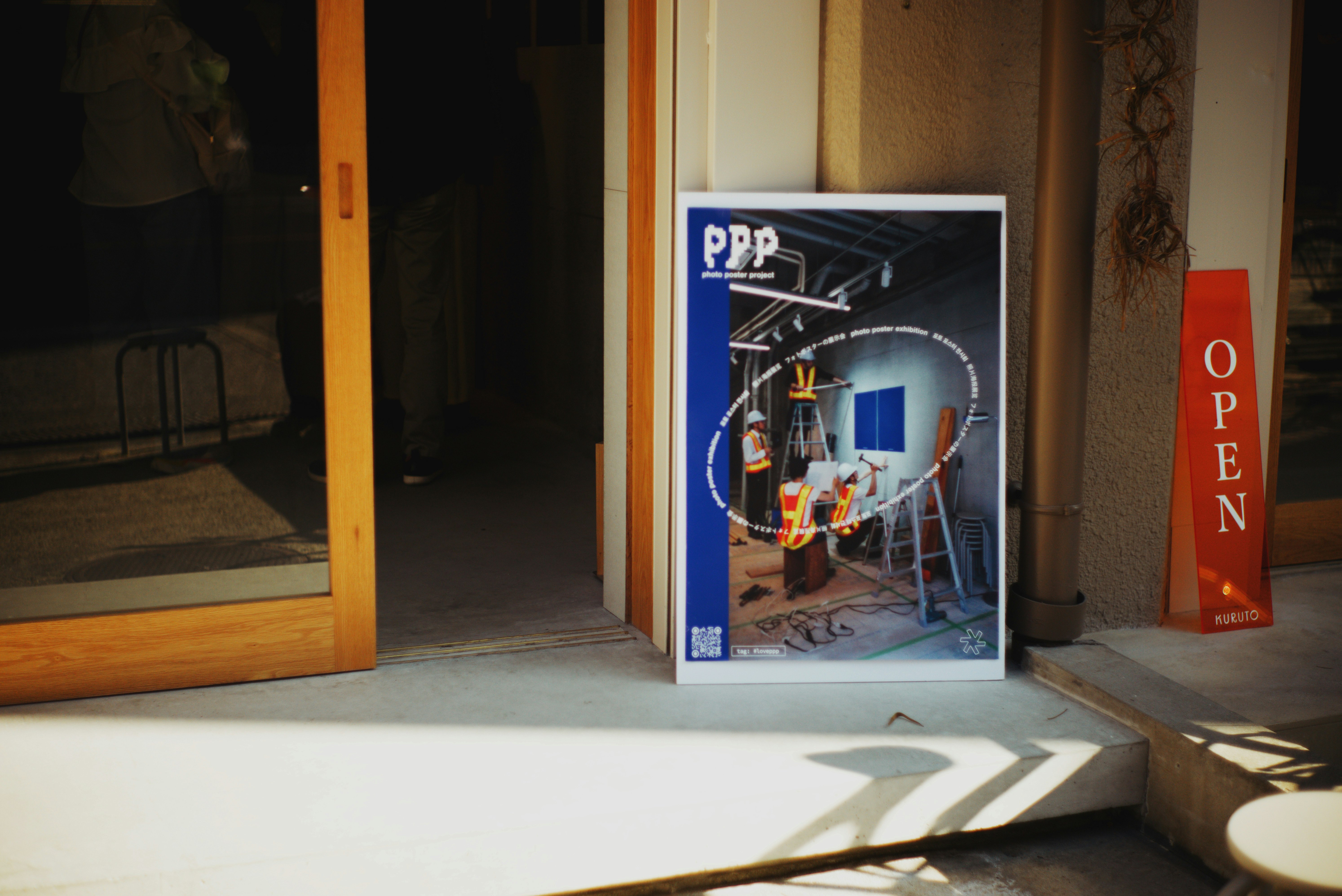 路地の壁に掲示された「ppp」ポスターと「OPEN」看板のある入口
