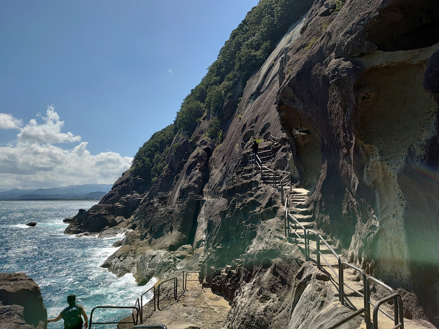 Sentiero roccioso lungo la costa con vista sull'oceano e vegetazione lussureggiante