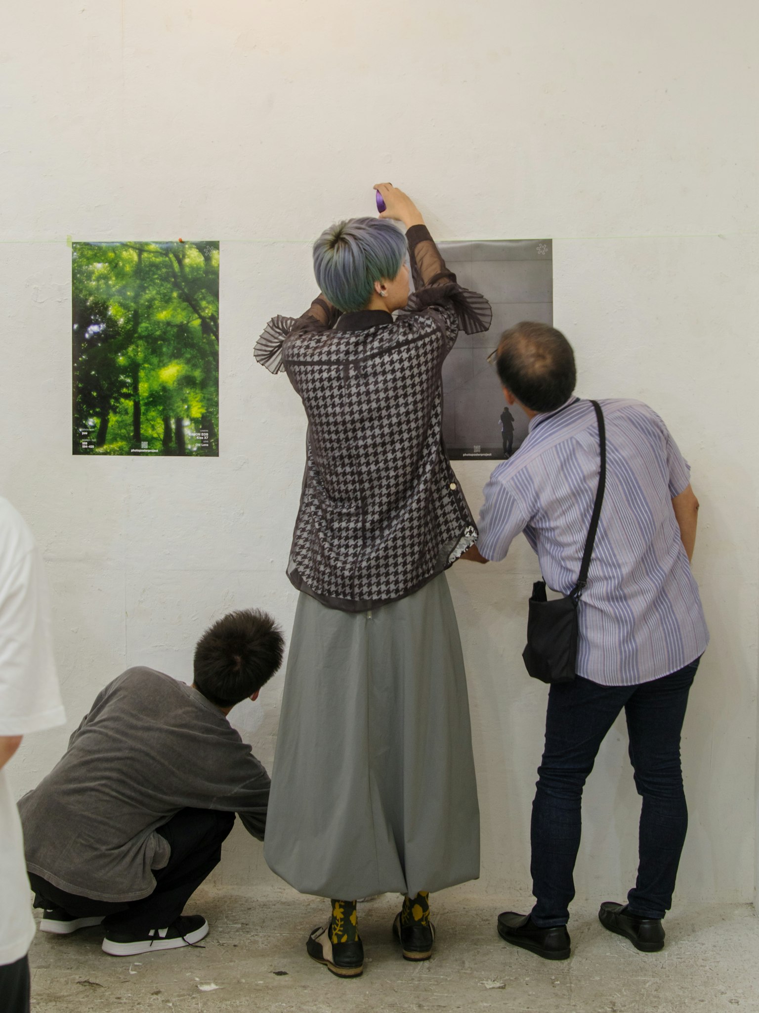 Menschen in einer Kunstgalerie, die Fotografien an einer Wand mit einer grünen Landschaft und einem anderen Kunstwerk aufhängen