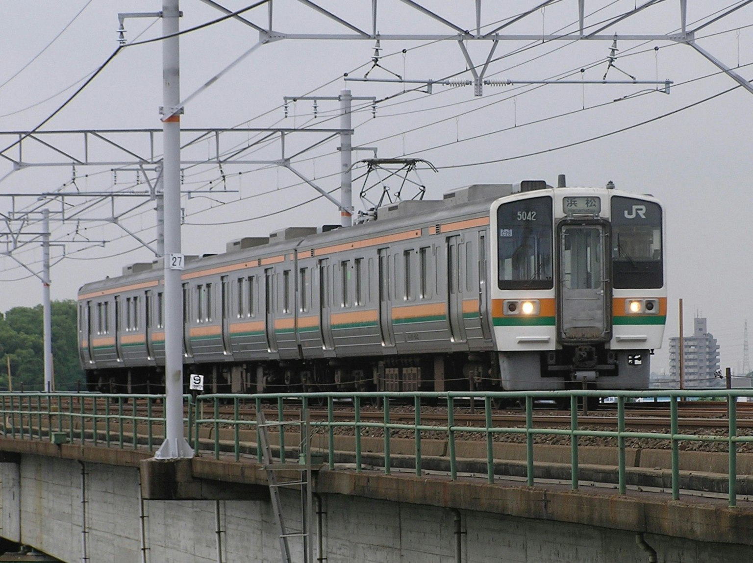 Tren circulando sobre un puente con vías y cables aéreos visibles