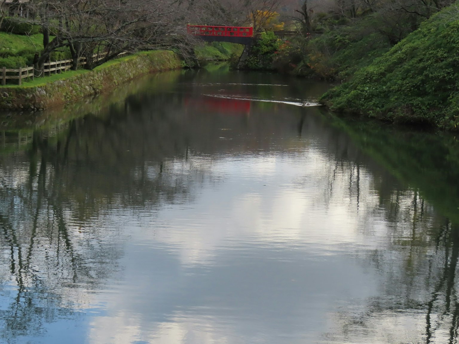 Scène de rivière calme avec réflexion d'un pont rouge et des nuages