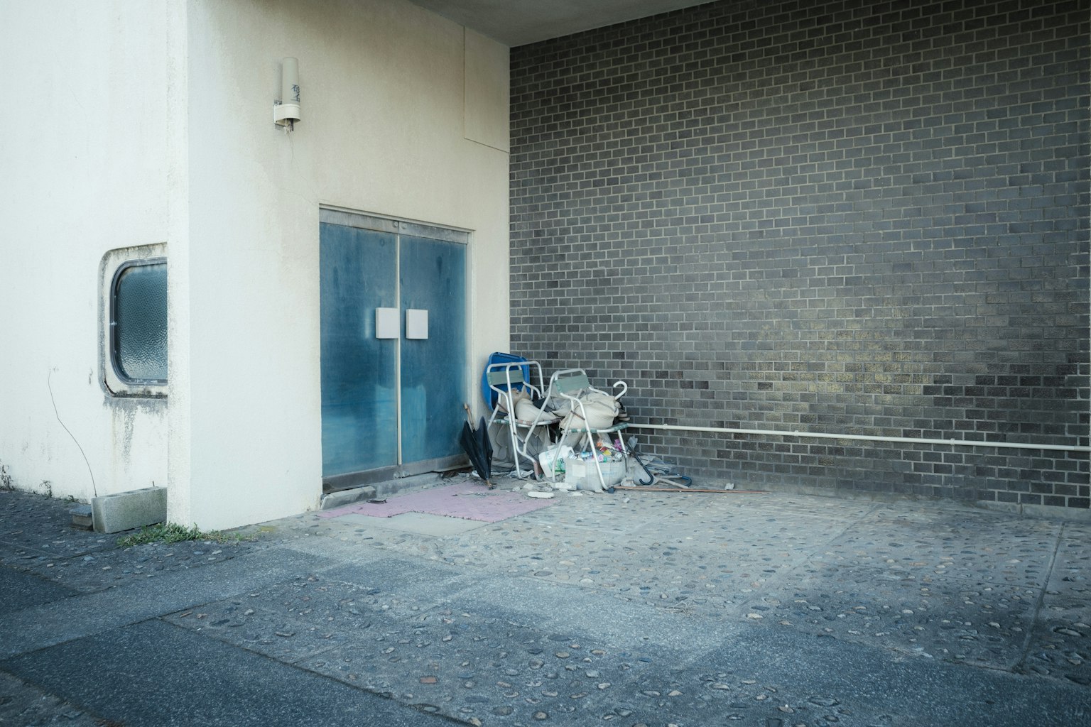Une porte bleue dans un coin de bâtiment avec un mur gris et des objets jetés à proximité