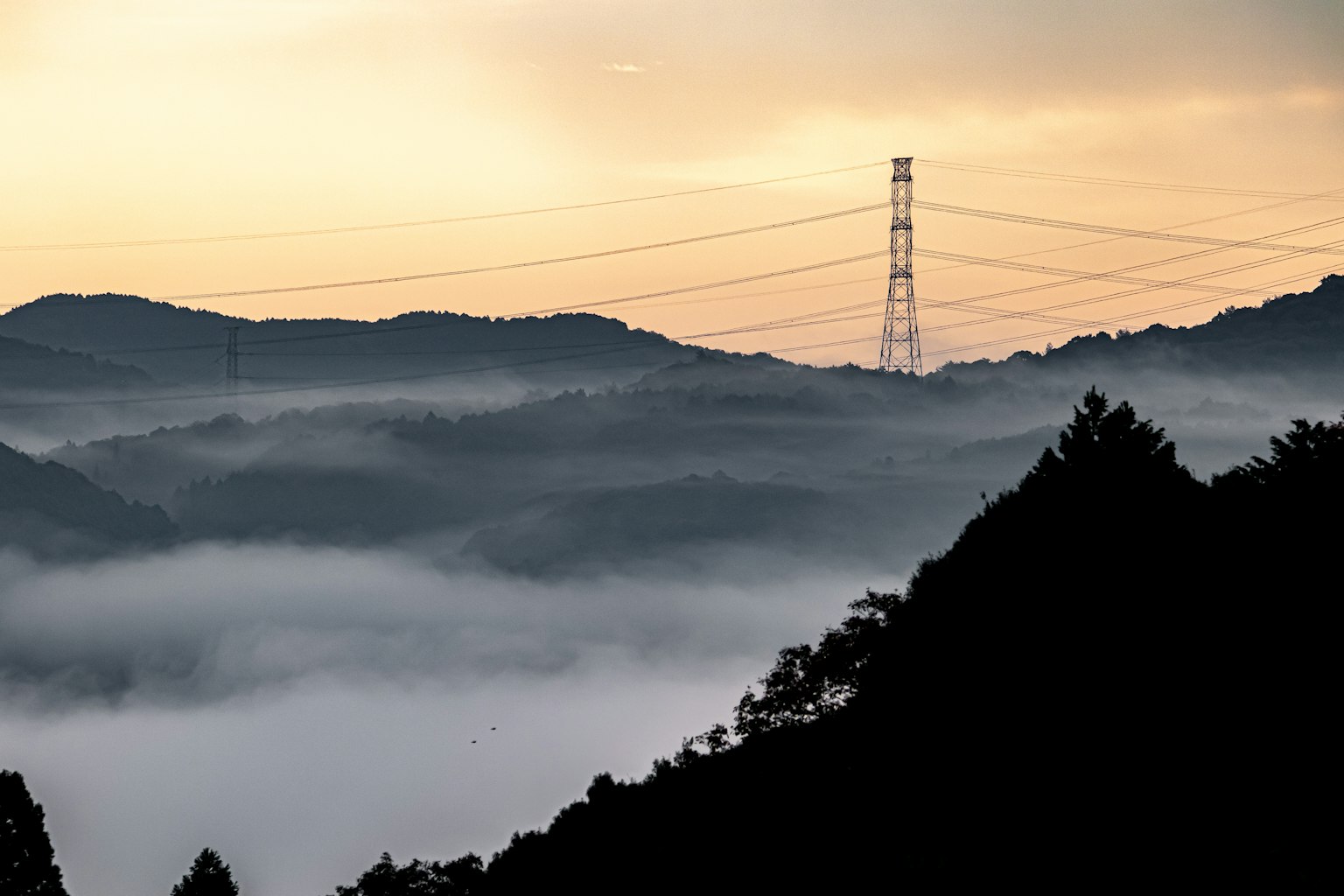 Montagnes en silhouette couvertes de brume avec un ciel au coucher de soleil et une haute tour électrique en arrière-plan