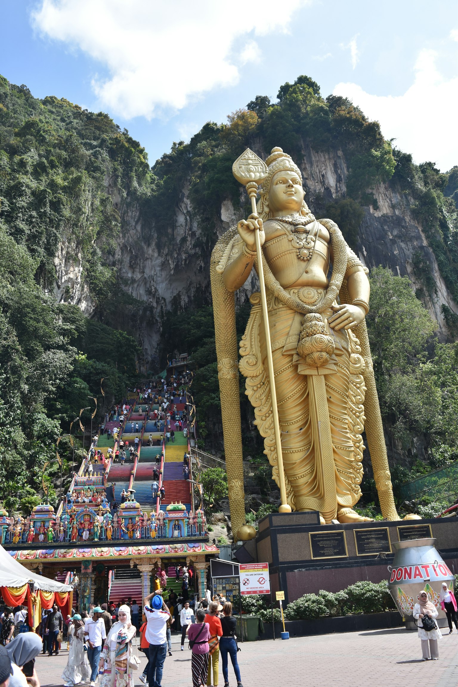 Giant golden Murugan statue at Batu Caves with colorful steps and tourists