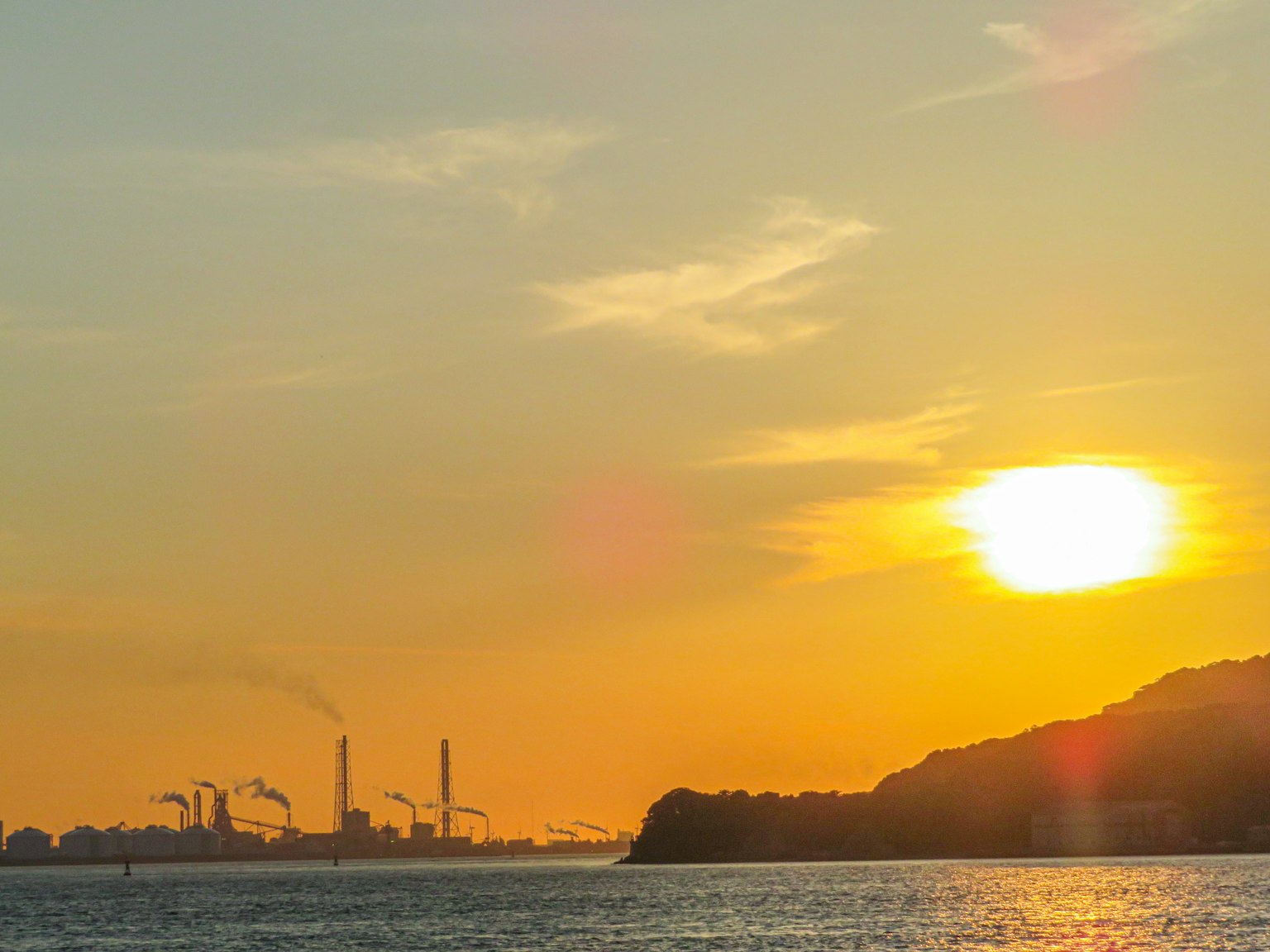 Industrielandschaft bei Sonnenuntergang mit Schornsteinen und Küstensilhouette