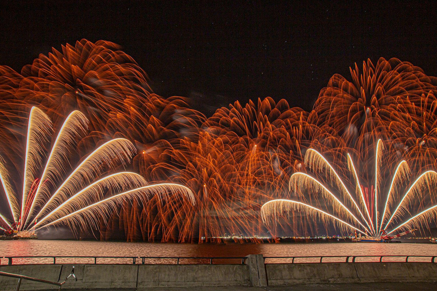 Vibrant orange fireworks spreading across the night sky reflecting on the water
