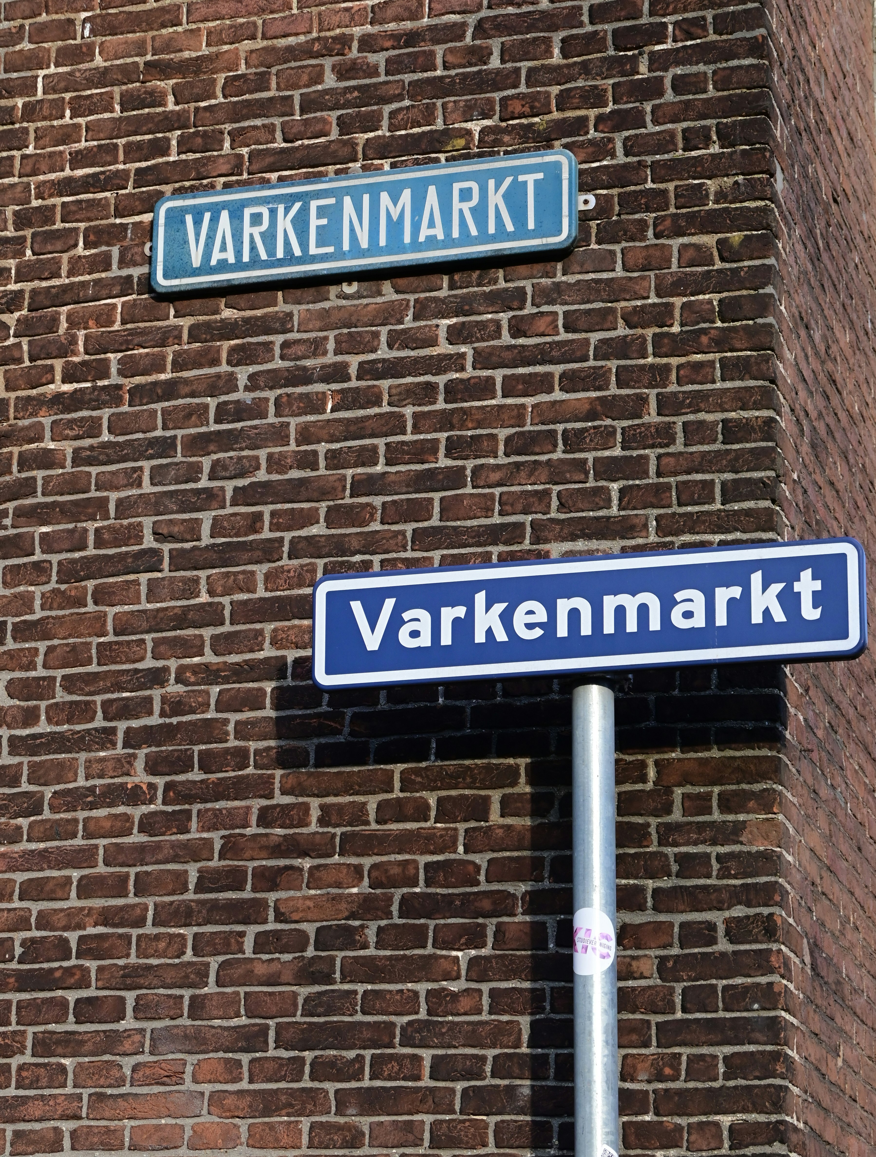 レンガ壁に取り付けられた「Varkenmarkt」の青い街路標識