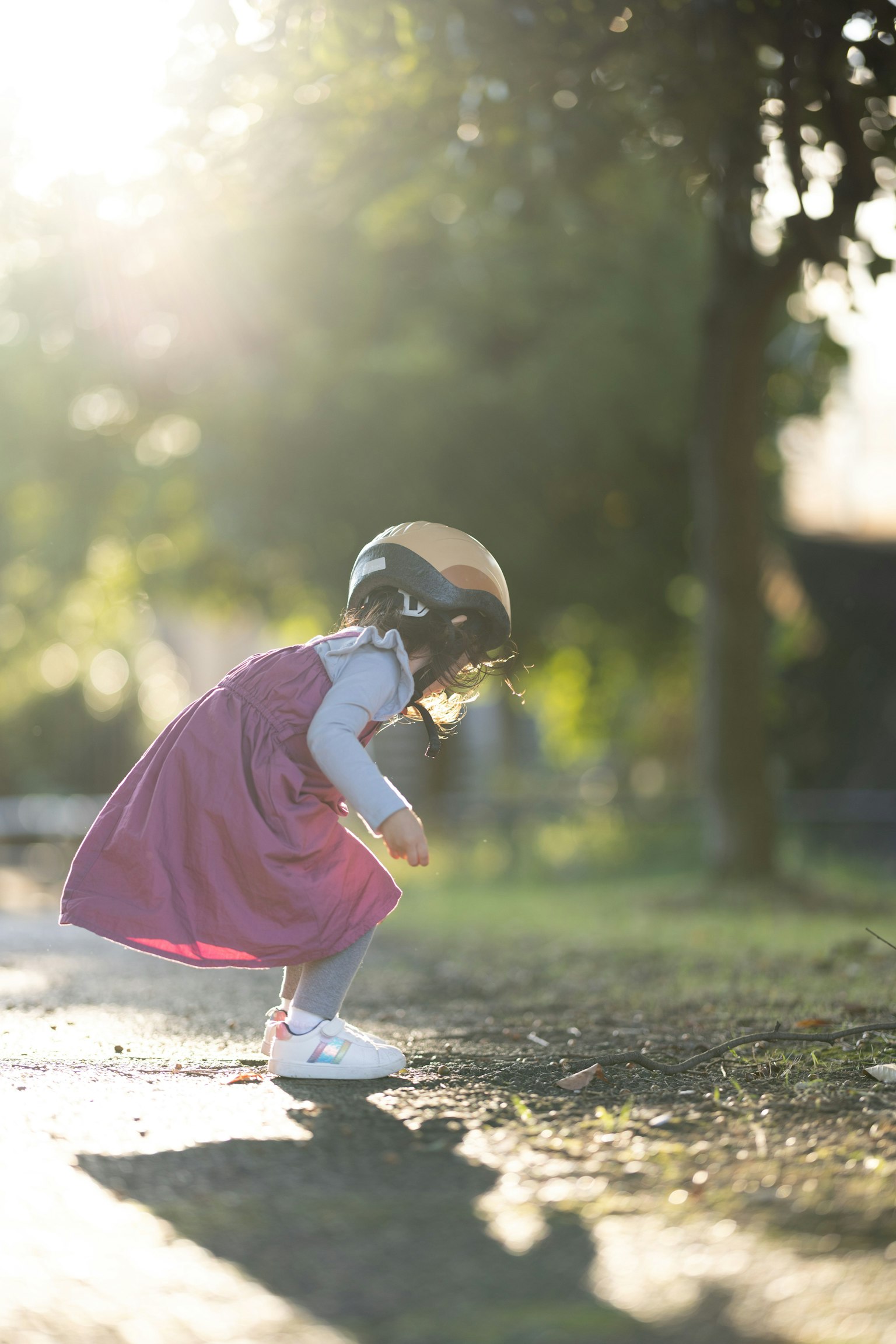 日差しの中で遊ぶ子供の女の子 ピンクのドレスとヘルメットを着用