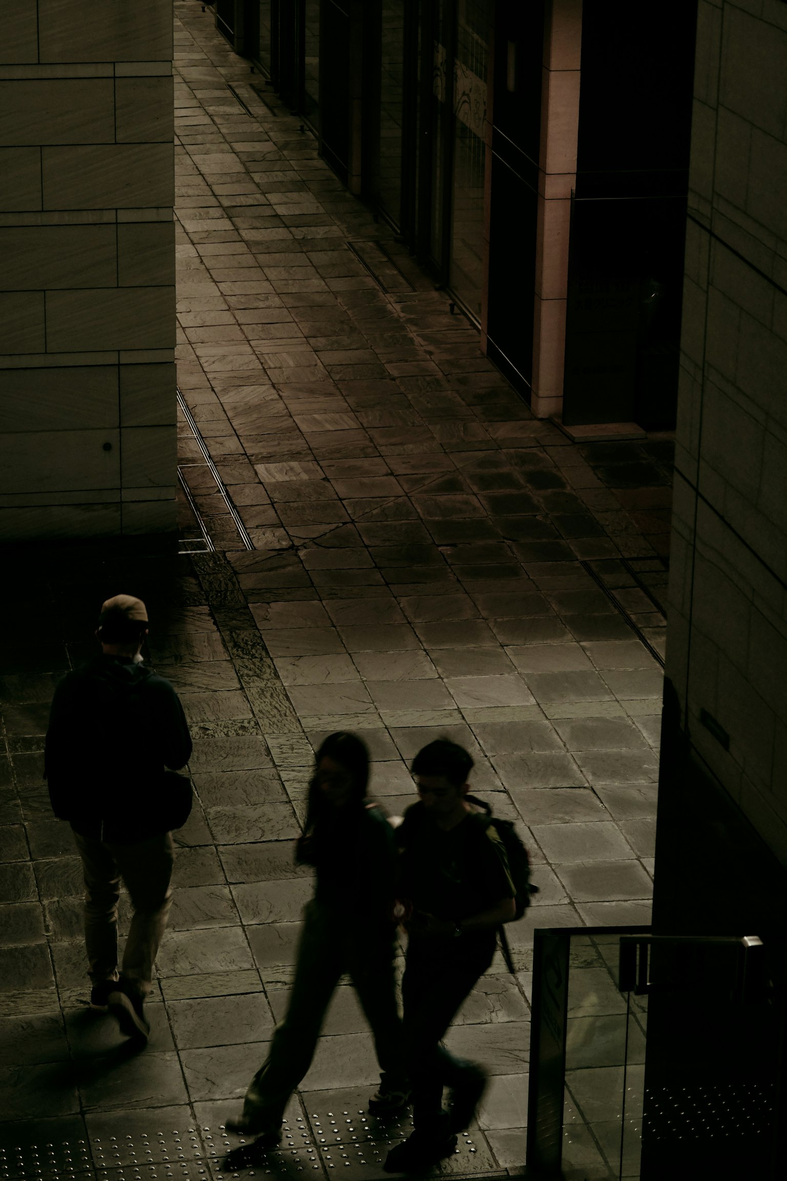 Silhouettes de deux personnes marchant dans une ruelle faiblement éclairée avec une autre personne en arrière-plan