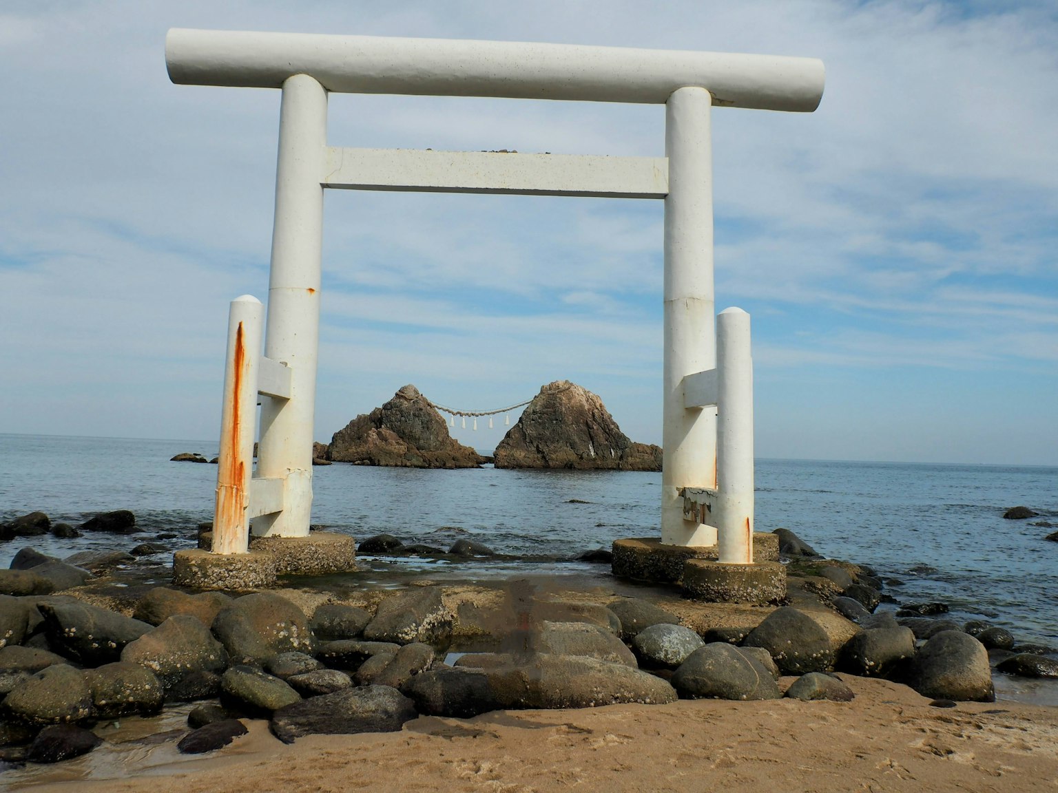 Weißes Torii steht zwischen Felsen am Meer