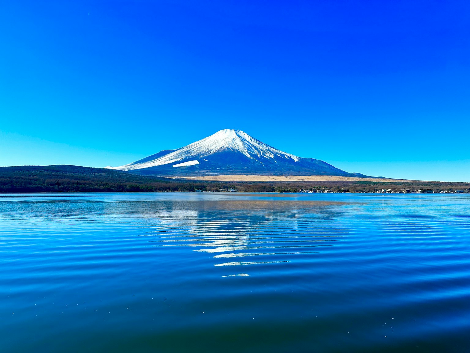 在晴朗藍天下聳立的富士山及其在水面上的倒影