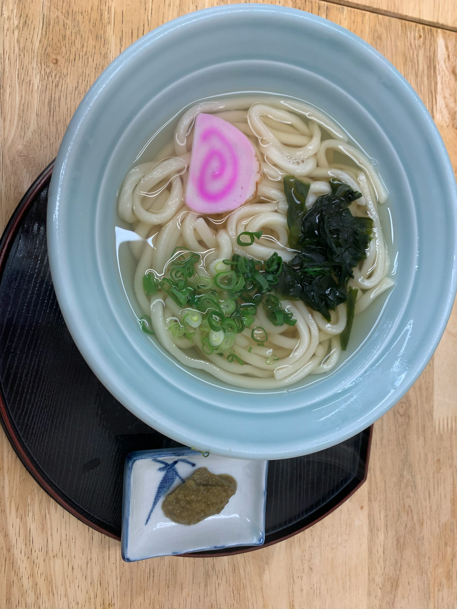 Mie udon dalam mangkuk biru dengan bawang hijau dan narutomaki merah muda