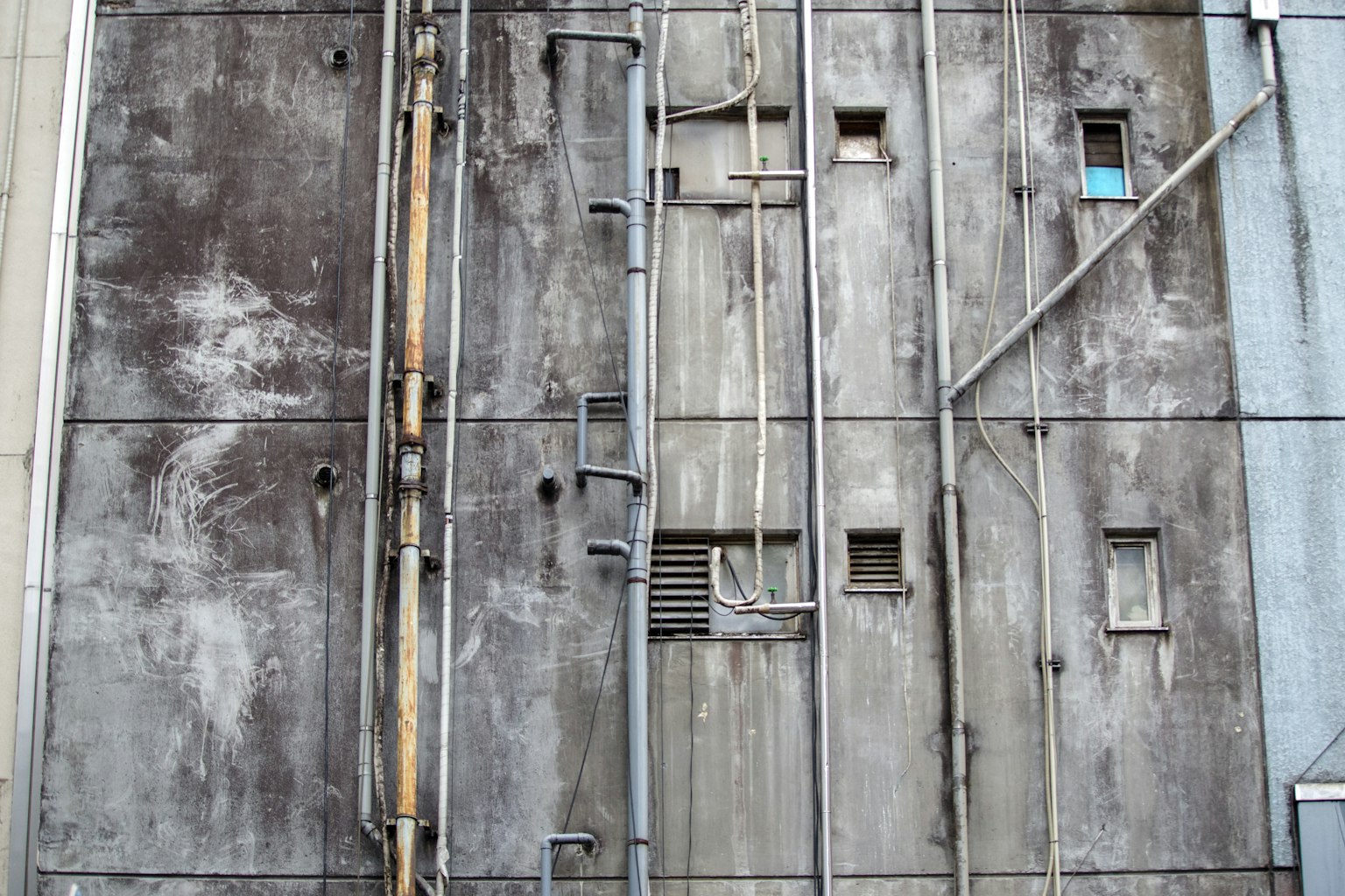 Industrial concrete wall featuring pipes and small windows