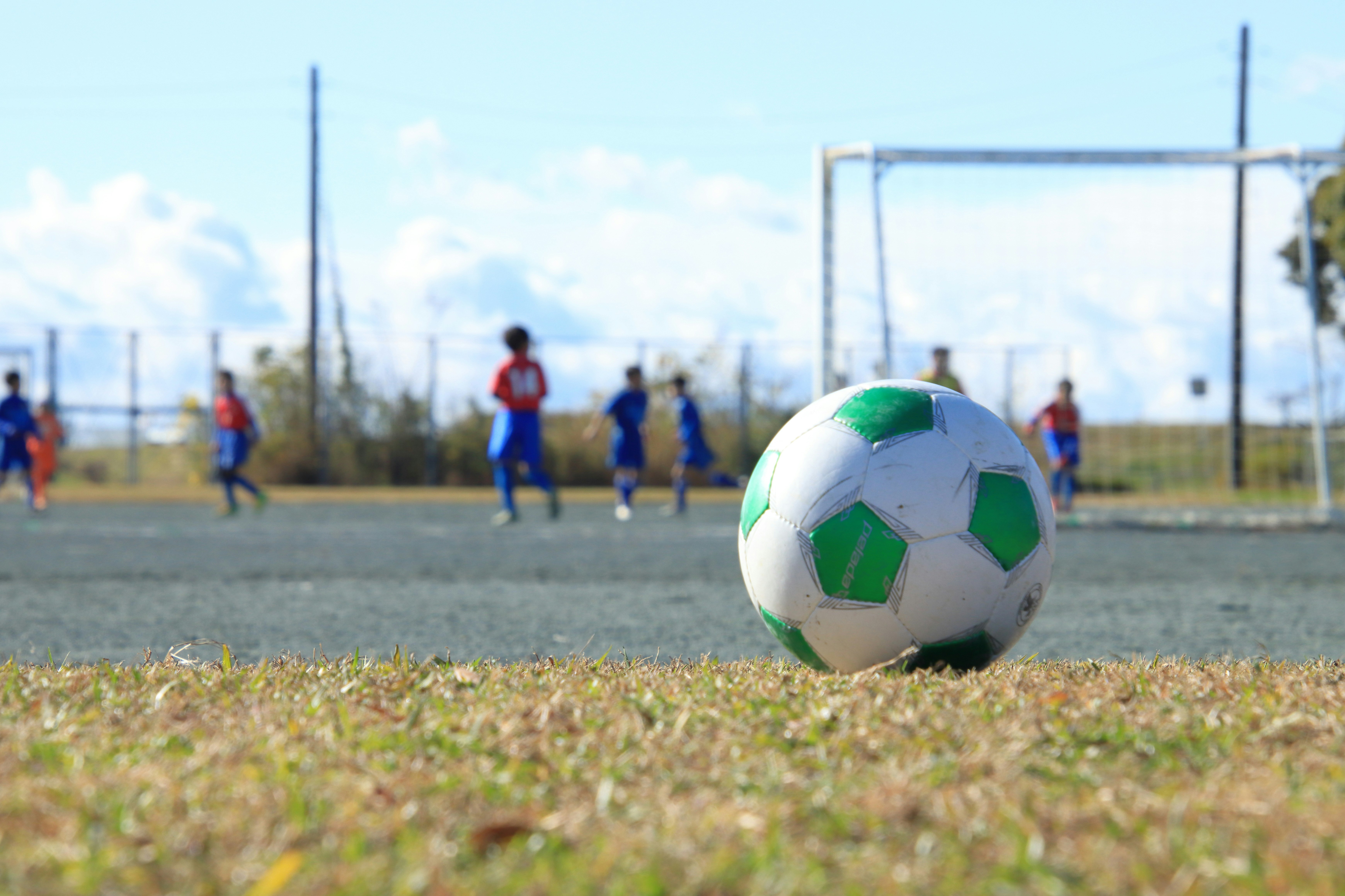 Fußball rollt auf Gras mit Tor im Hintergrund