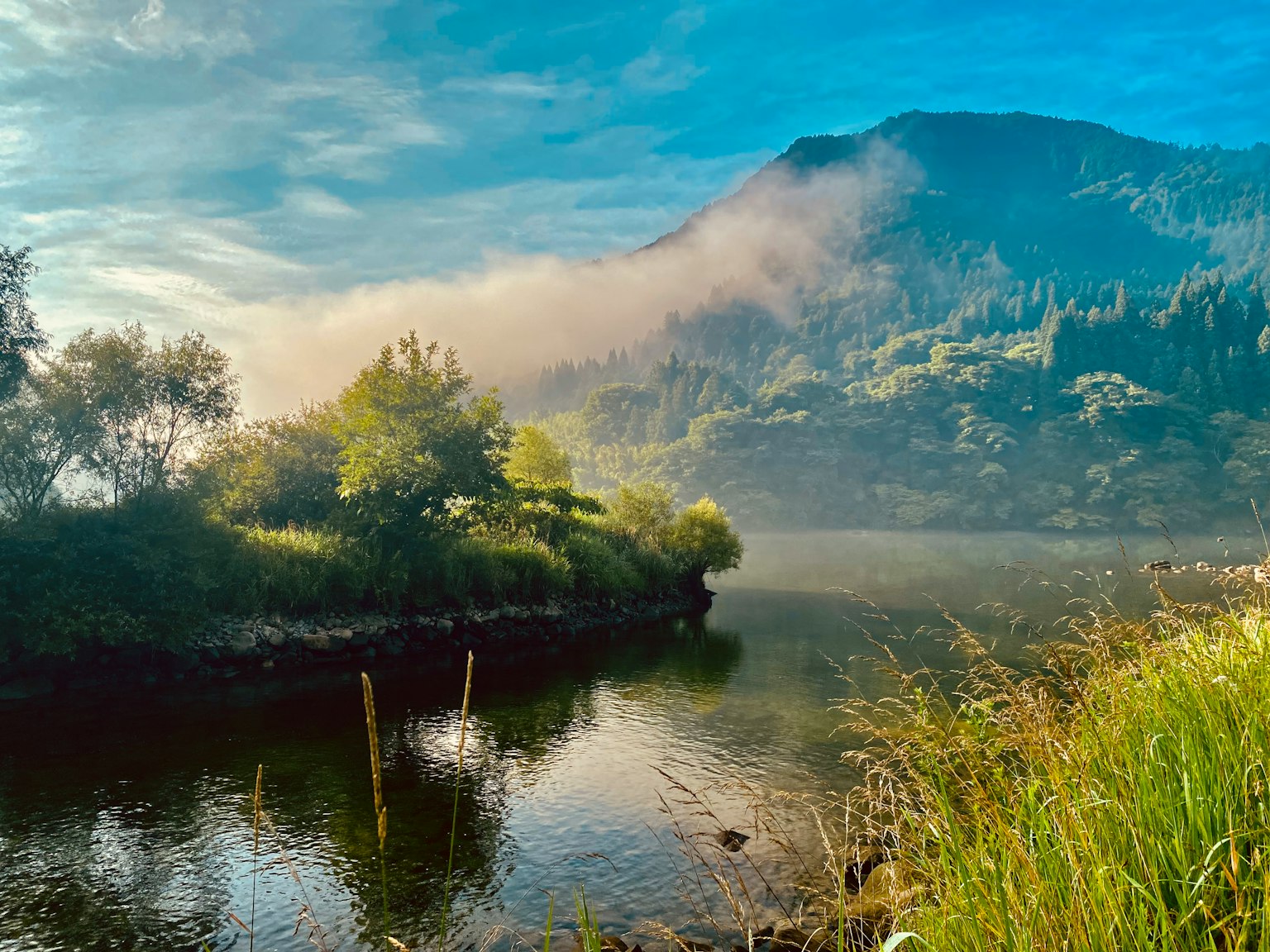 Vista escénica de una montaña brumosa y un lago tranquilo rodeado de vegetación exuberante