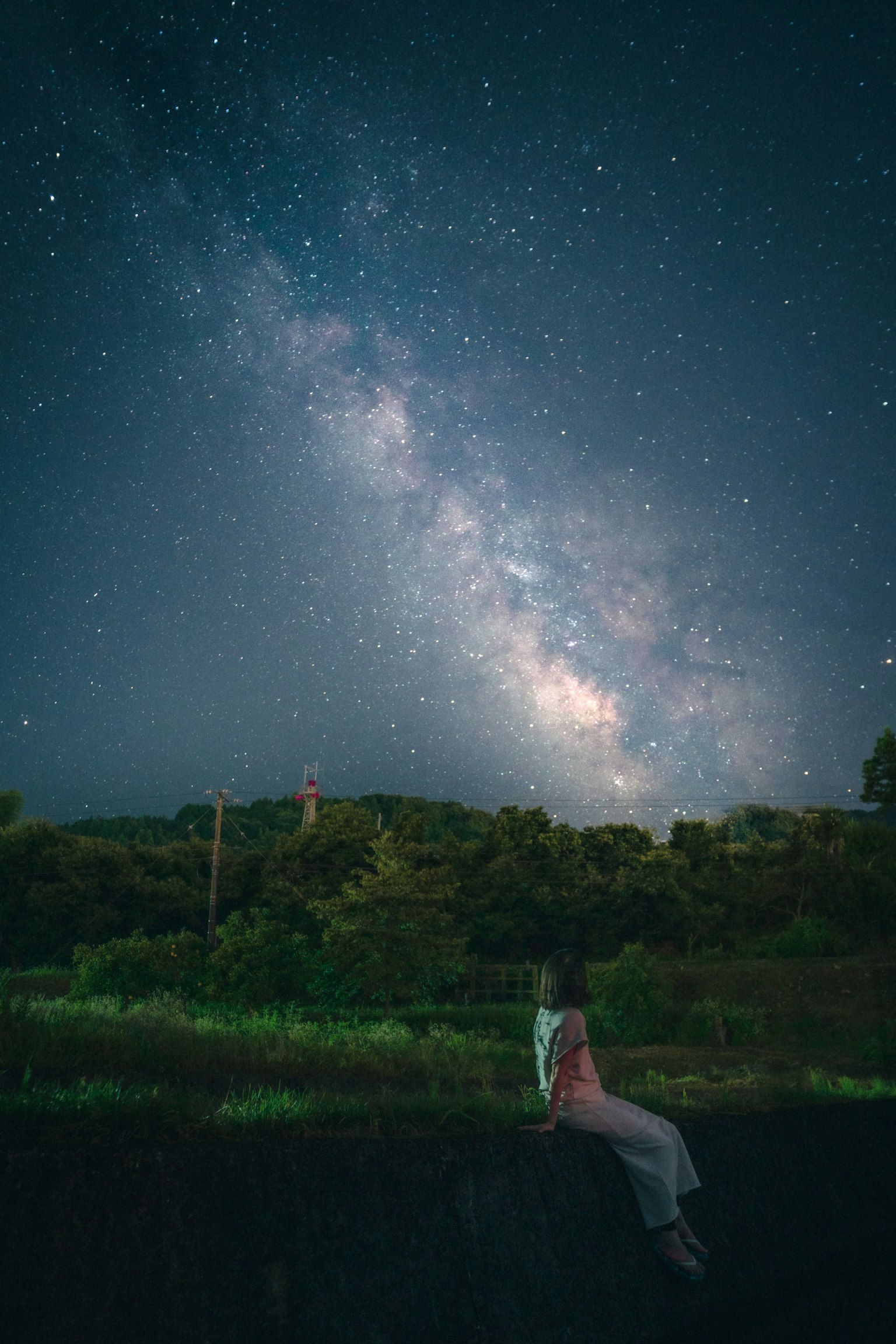 A woman sitting under a starry sky with a beautiful view of the Milky Way