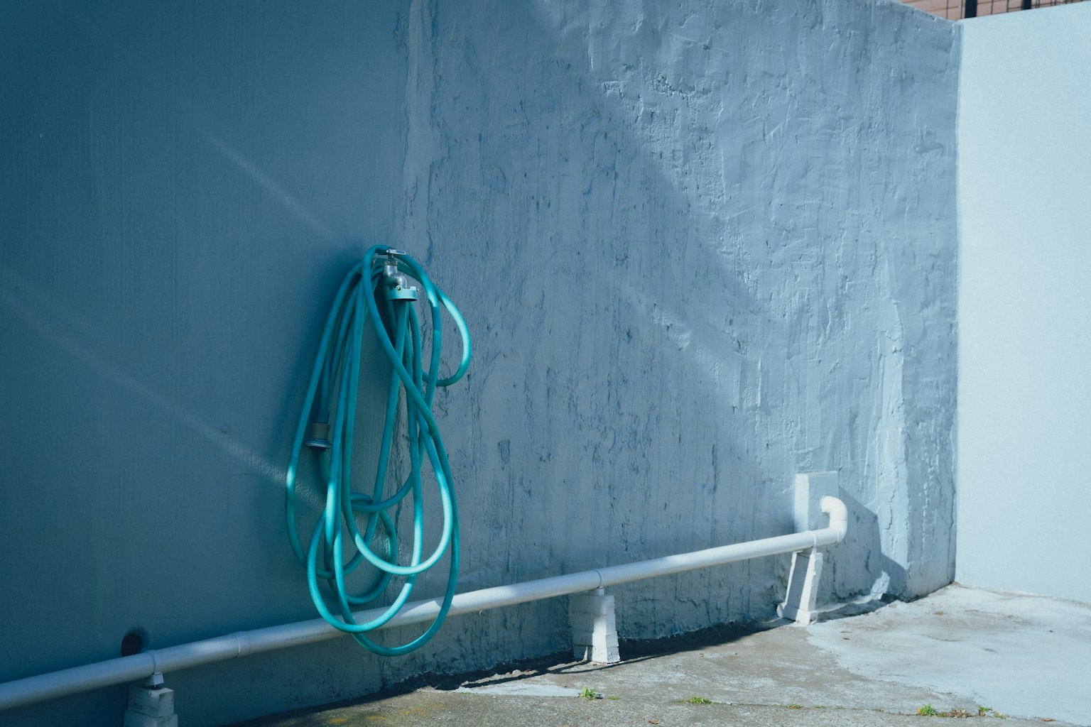 Green garden hose hanging on a light blue wall with white piping