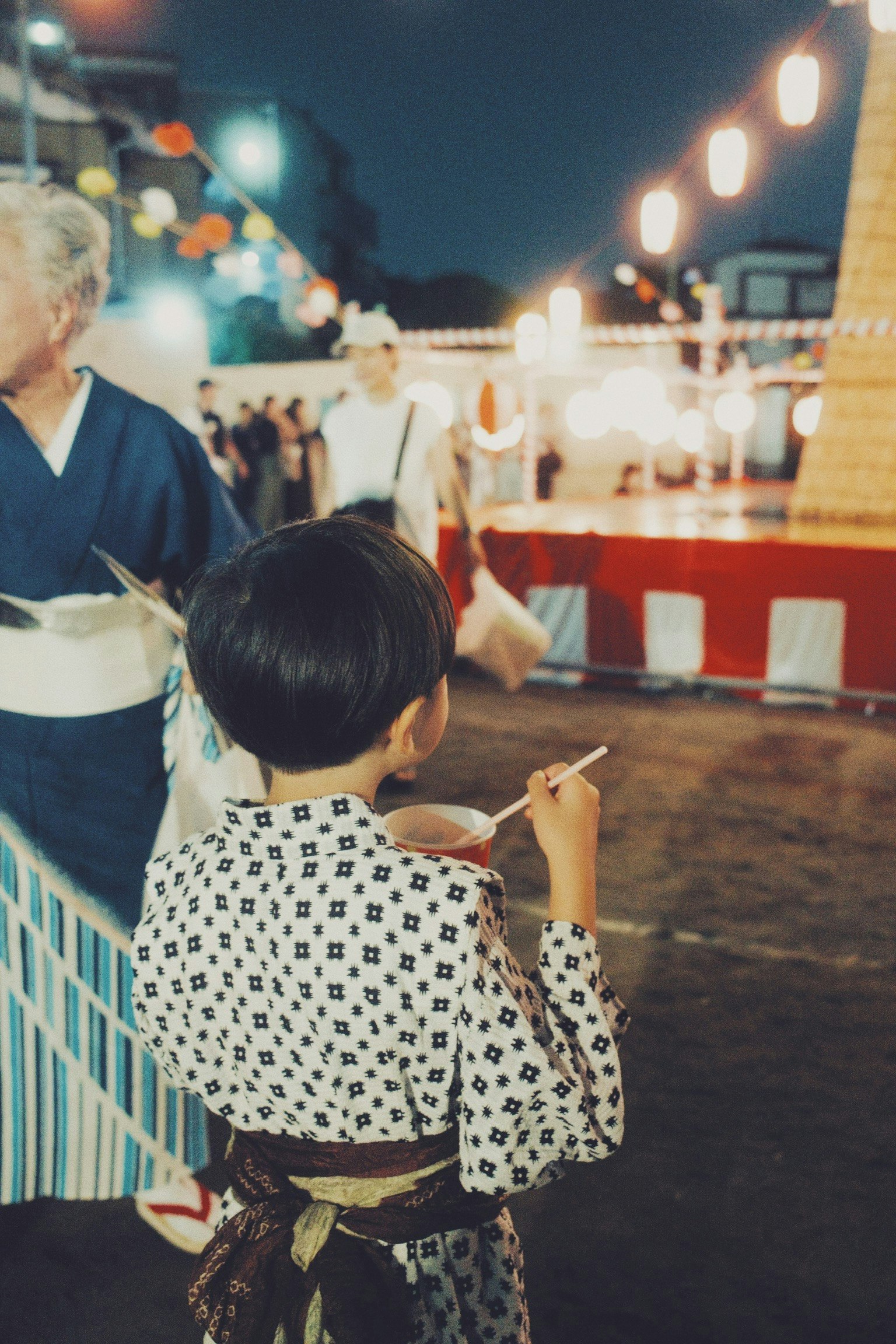 Bambino in yukata che tiene del cibo a un festival notturno