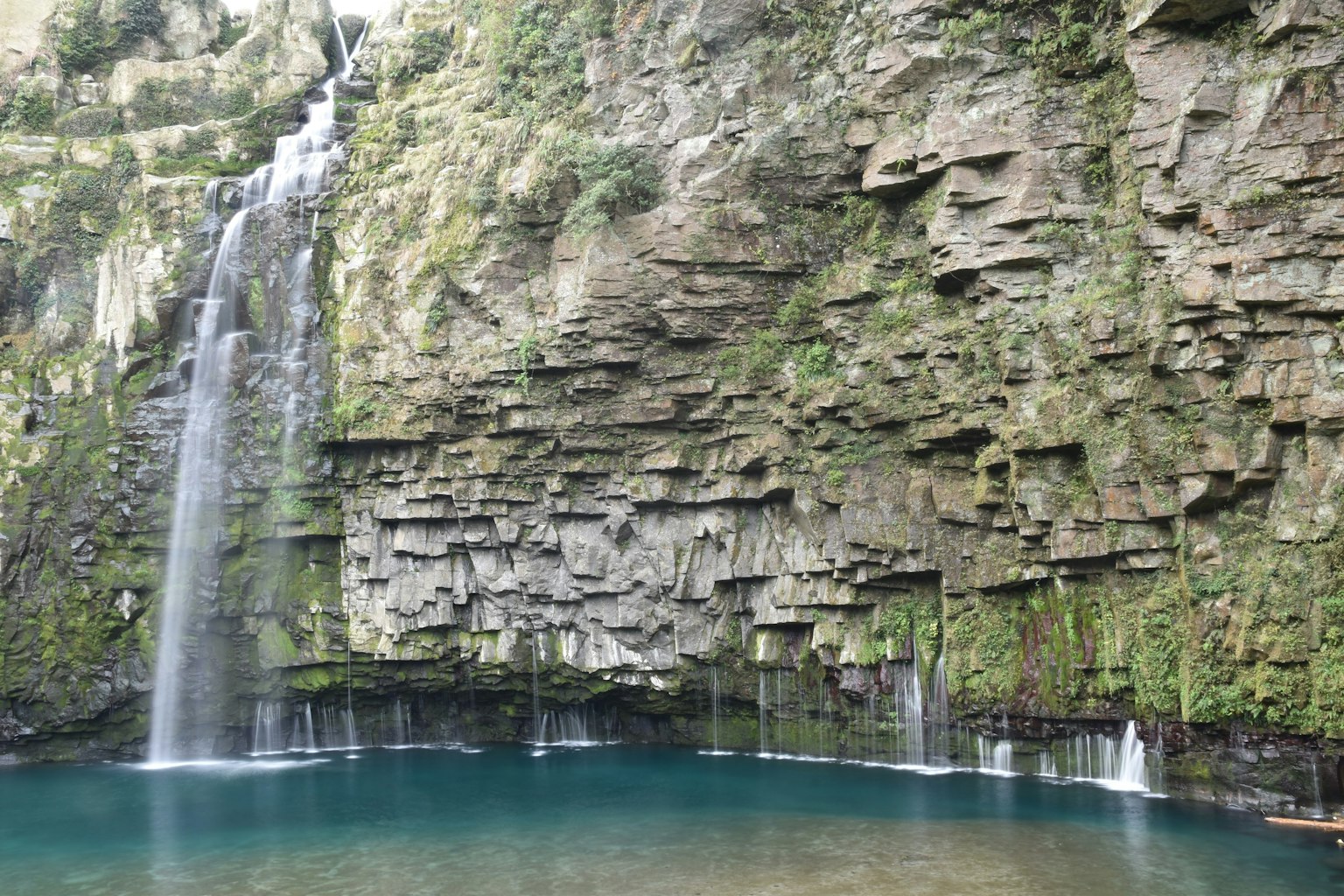 Una bellissima cascata che scende da una scogliera rocciosa circondata da muschio verde e una tranquilla pozza blu