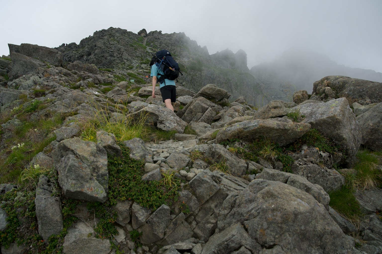 Escursionista che sale su un sentiero roccioso avvolto nella nebbia