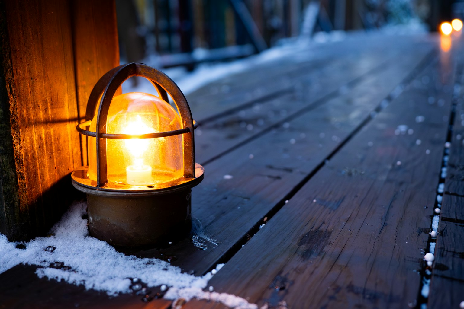 Warm orange lantern on snowy wooden deck at dusk