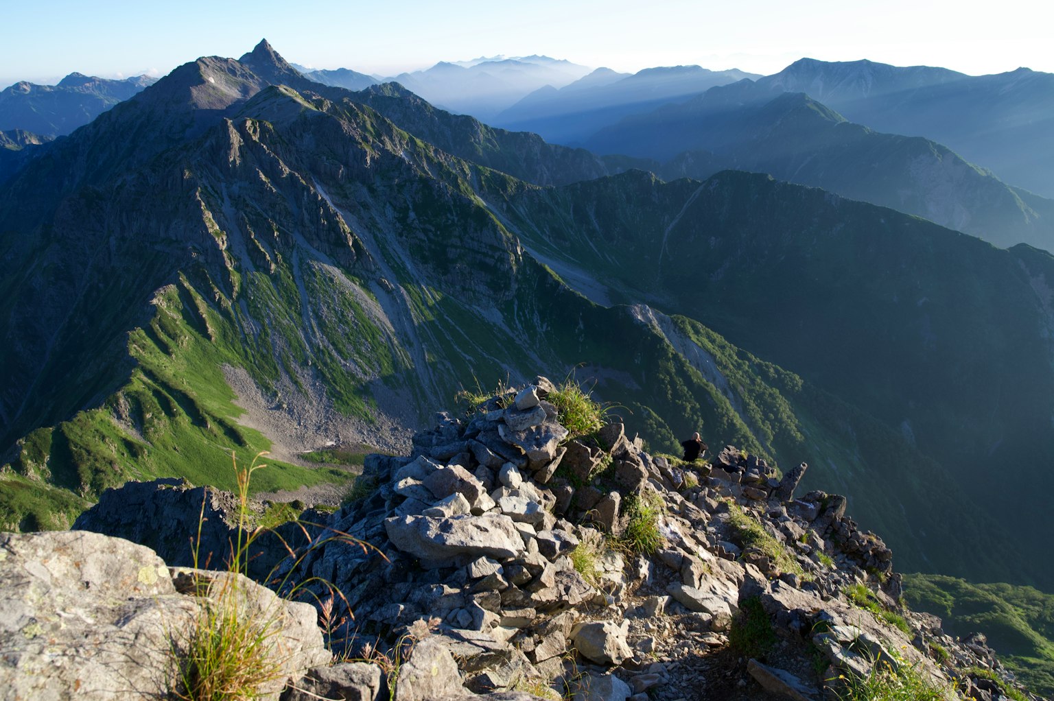 Panoramic view from mountain peak featuring green slopes and distant mountains
