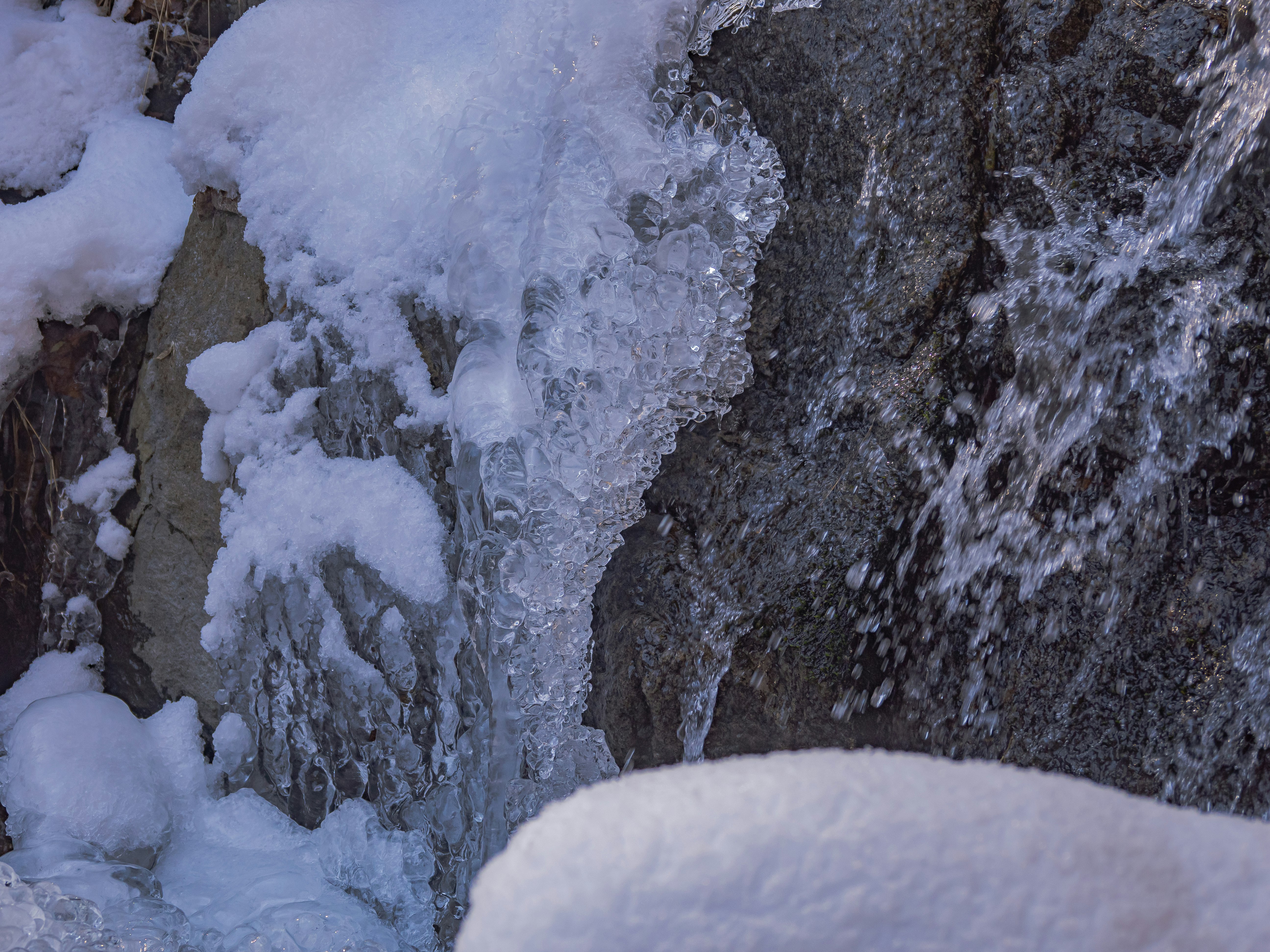 雪の積もる岩肌と流れる小さな滝の水