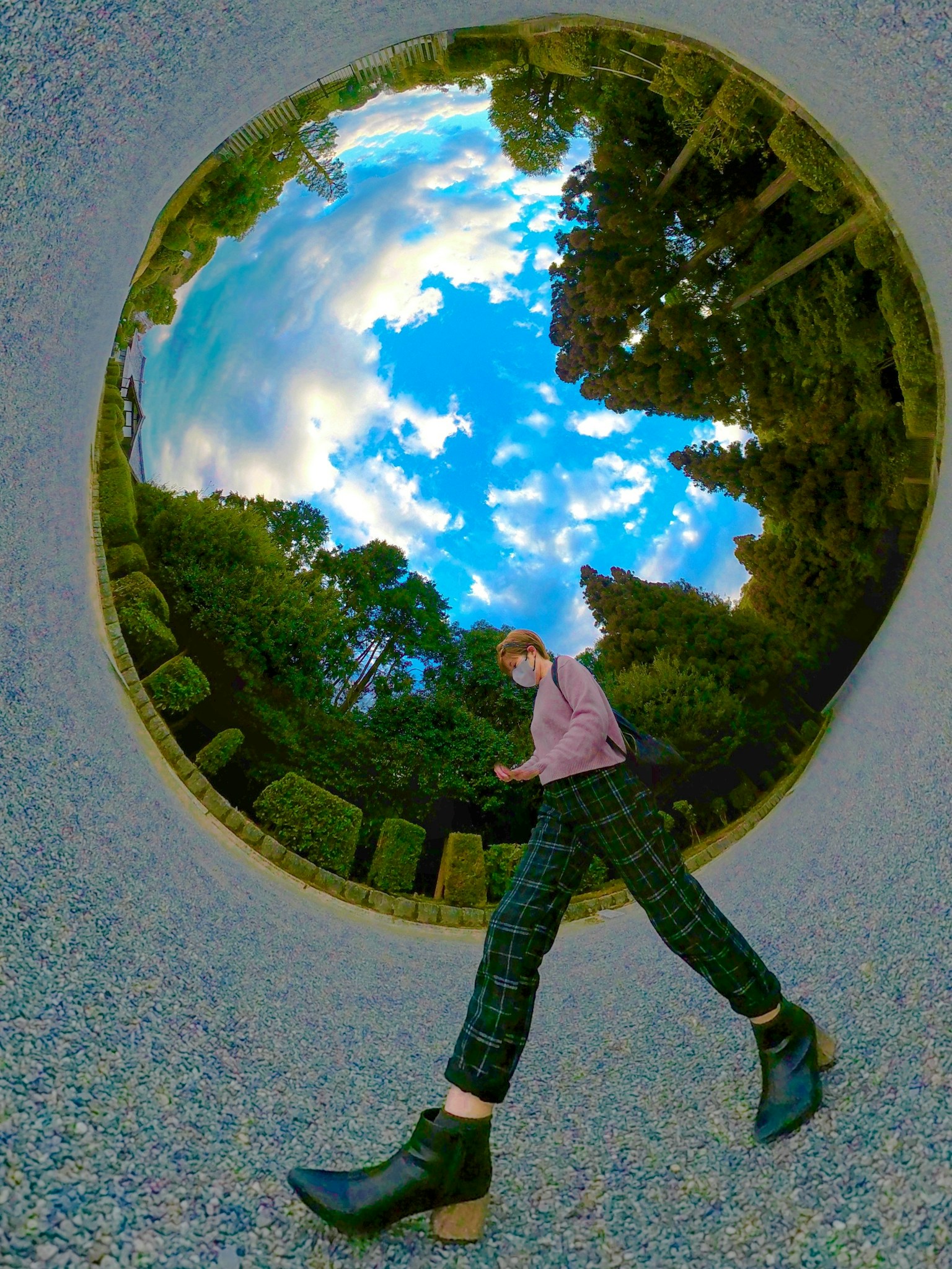 一個人在圓形框架中行走，藍天和綠色樹木的倒影