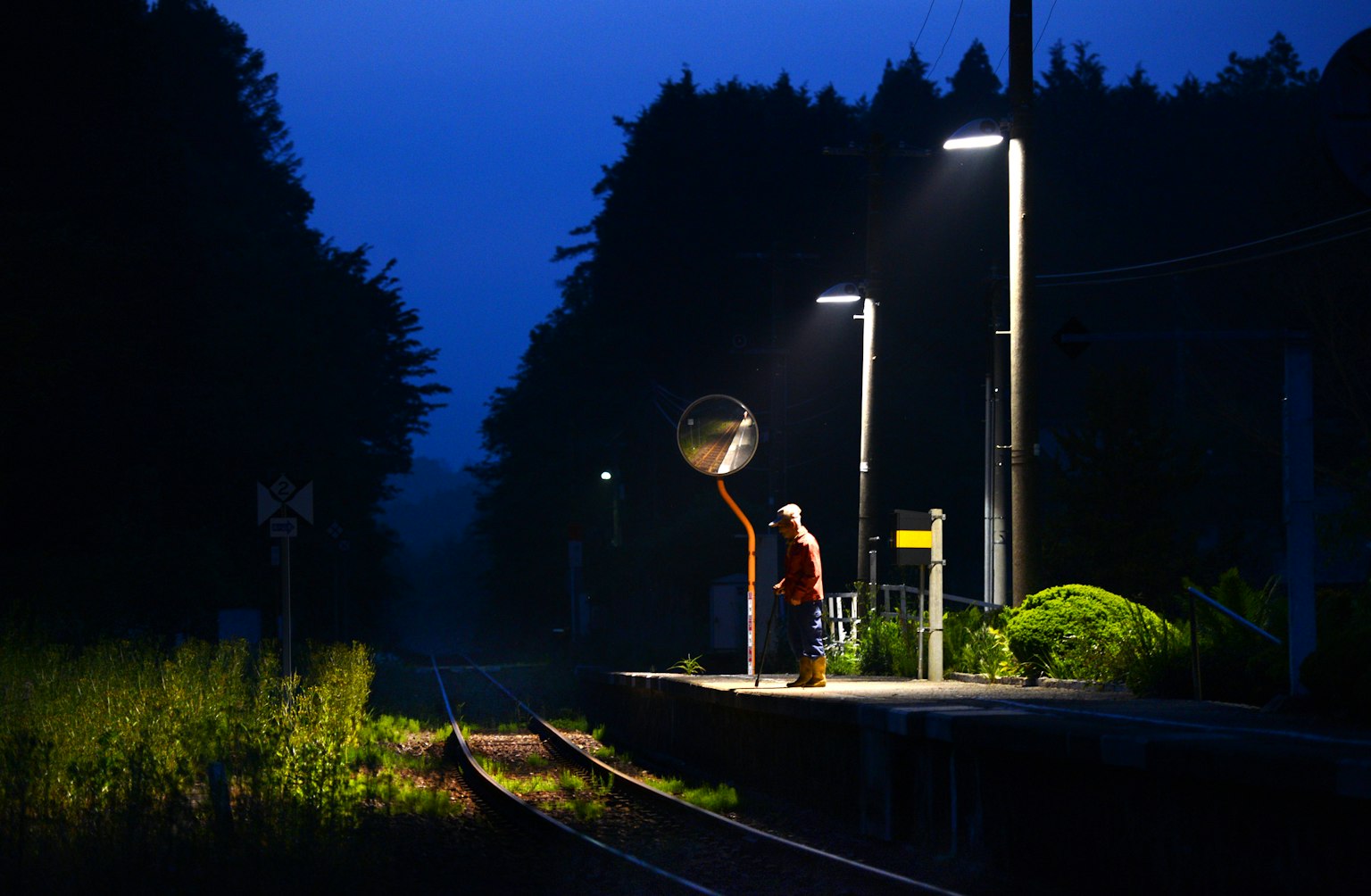 Une personne se tenant sur un quai de train la nuit avec des lumières environnantes