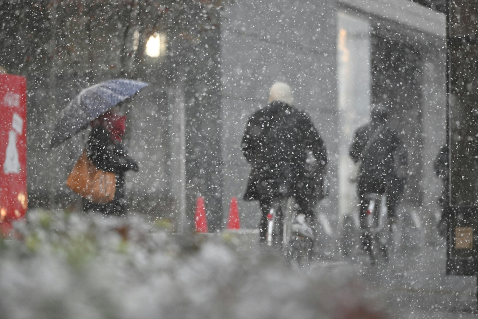People cycling in the snow with a woman holding an umbrella