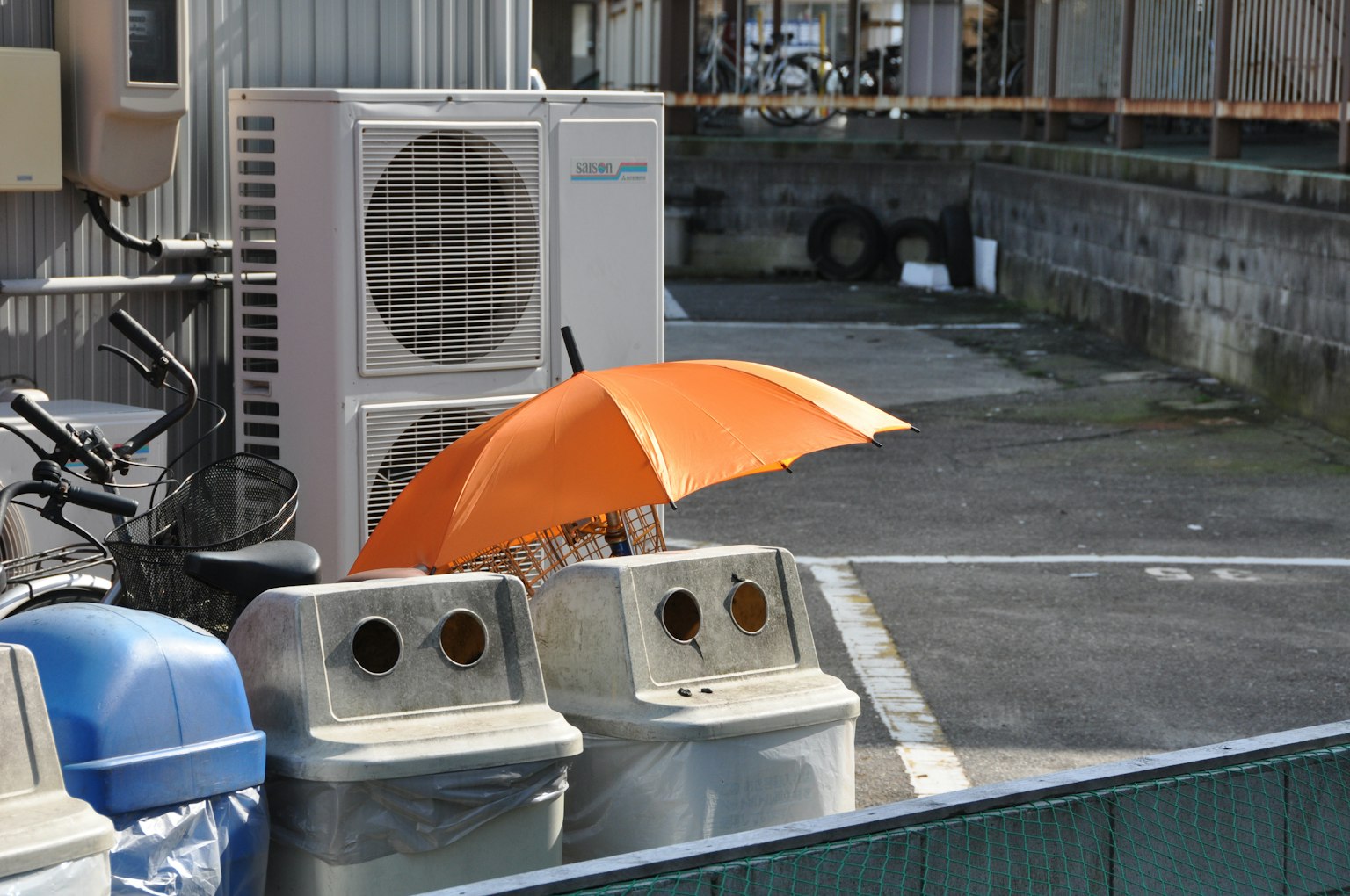 一個場景，展示了一個垃圾桶和一把橙色雨傘以及一個空調單元