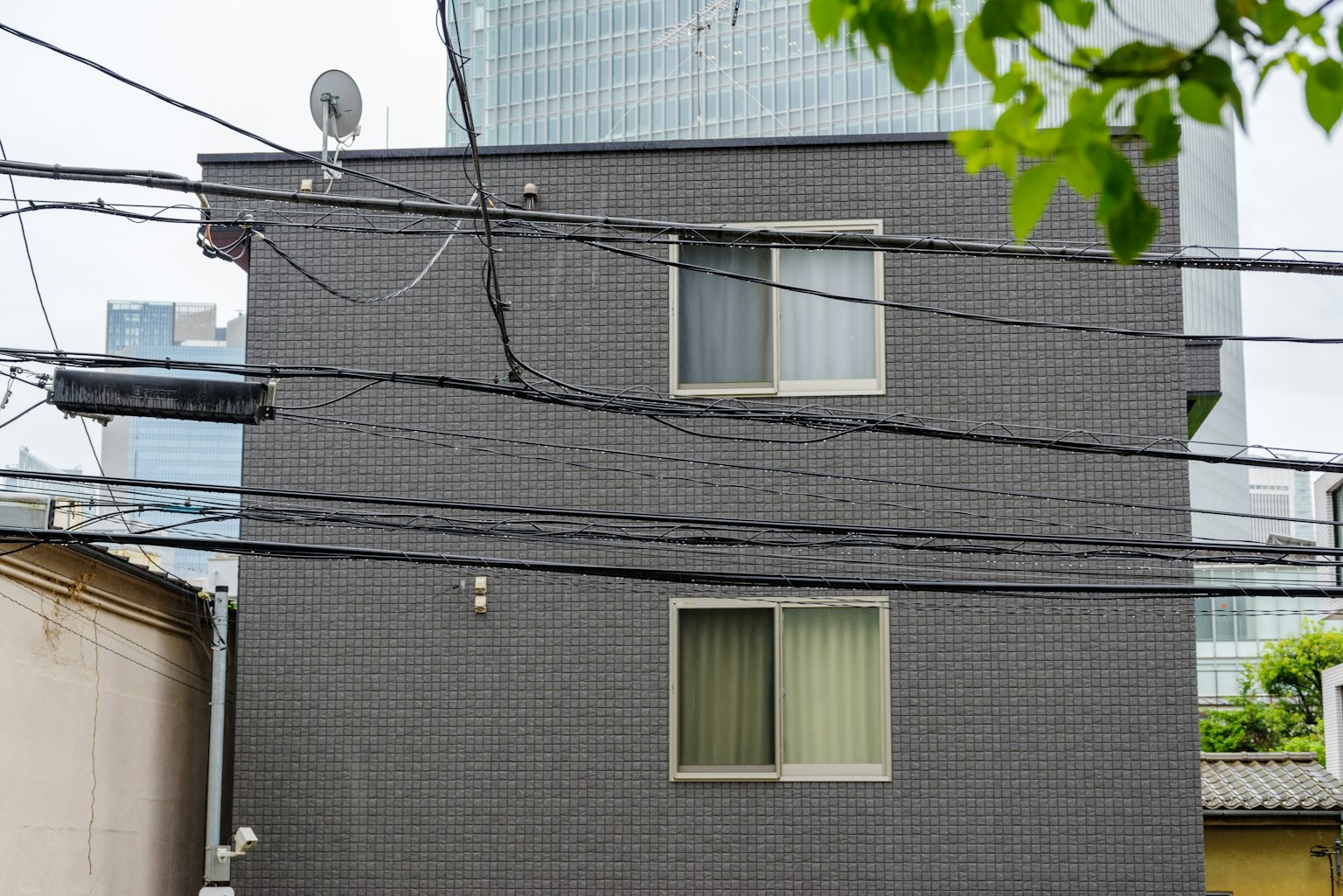 Edificio de dos pisos con exterior oscuro y líneas eléctricas en un entorno urbano