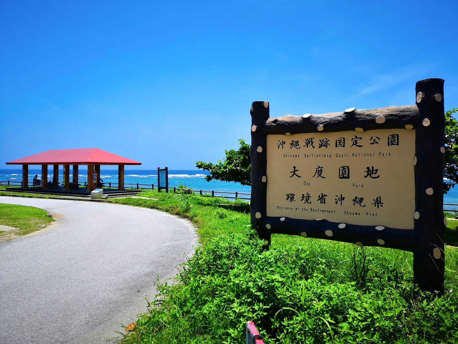 Park sign with red-roofed pavilion against blue sky and sea