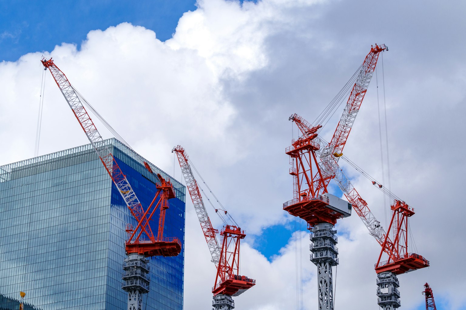 Sitio de construcción con grúas rojas y blancas bajo un cielo azul