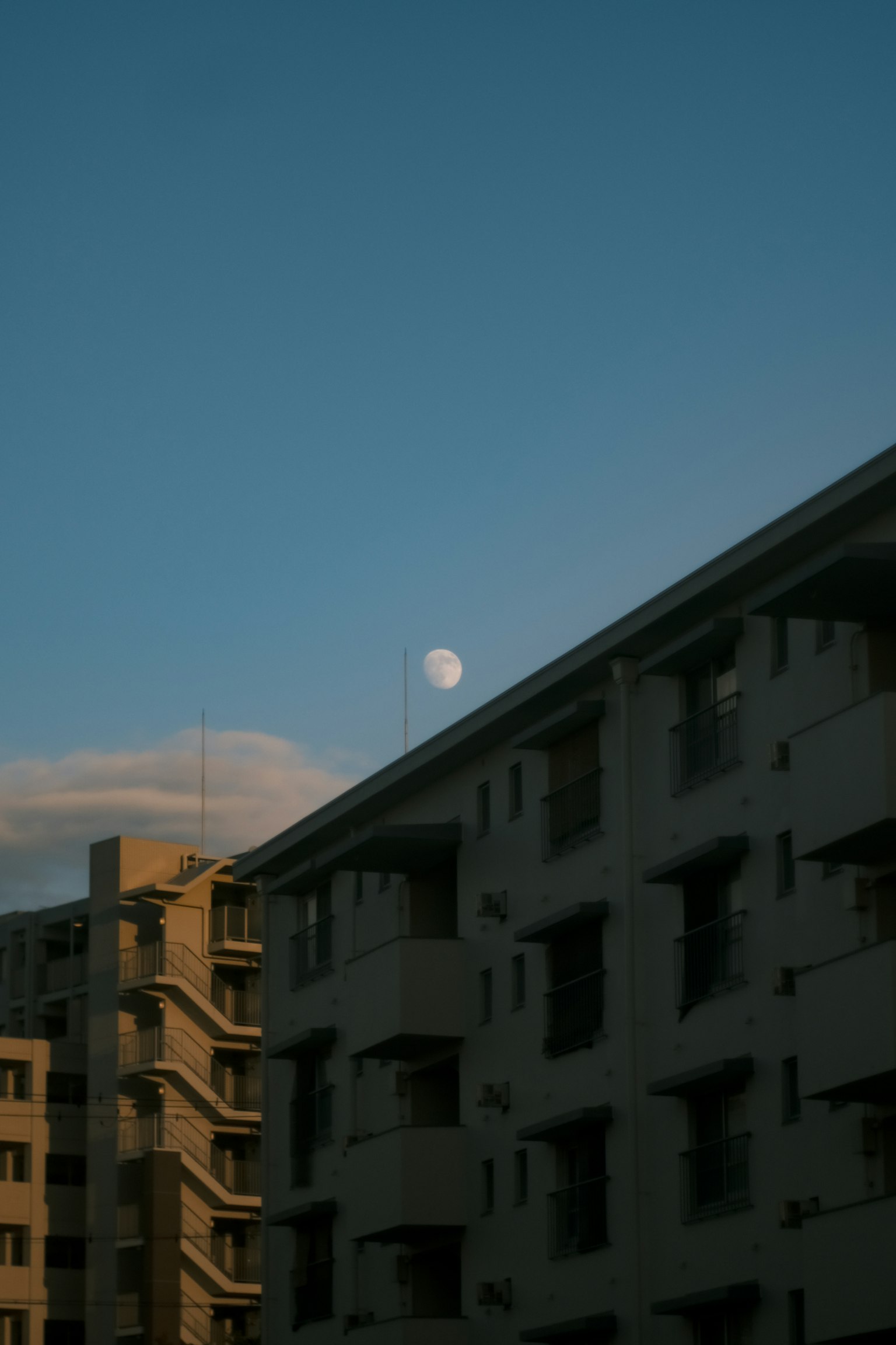 青空に浮かぶ月と建物のシルエット