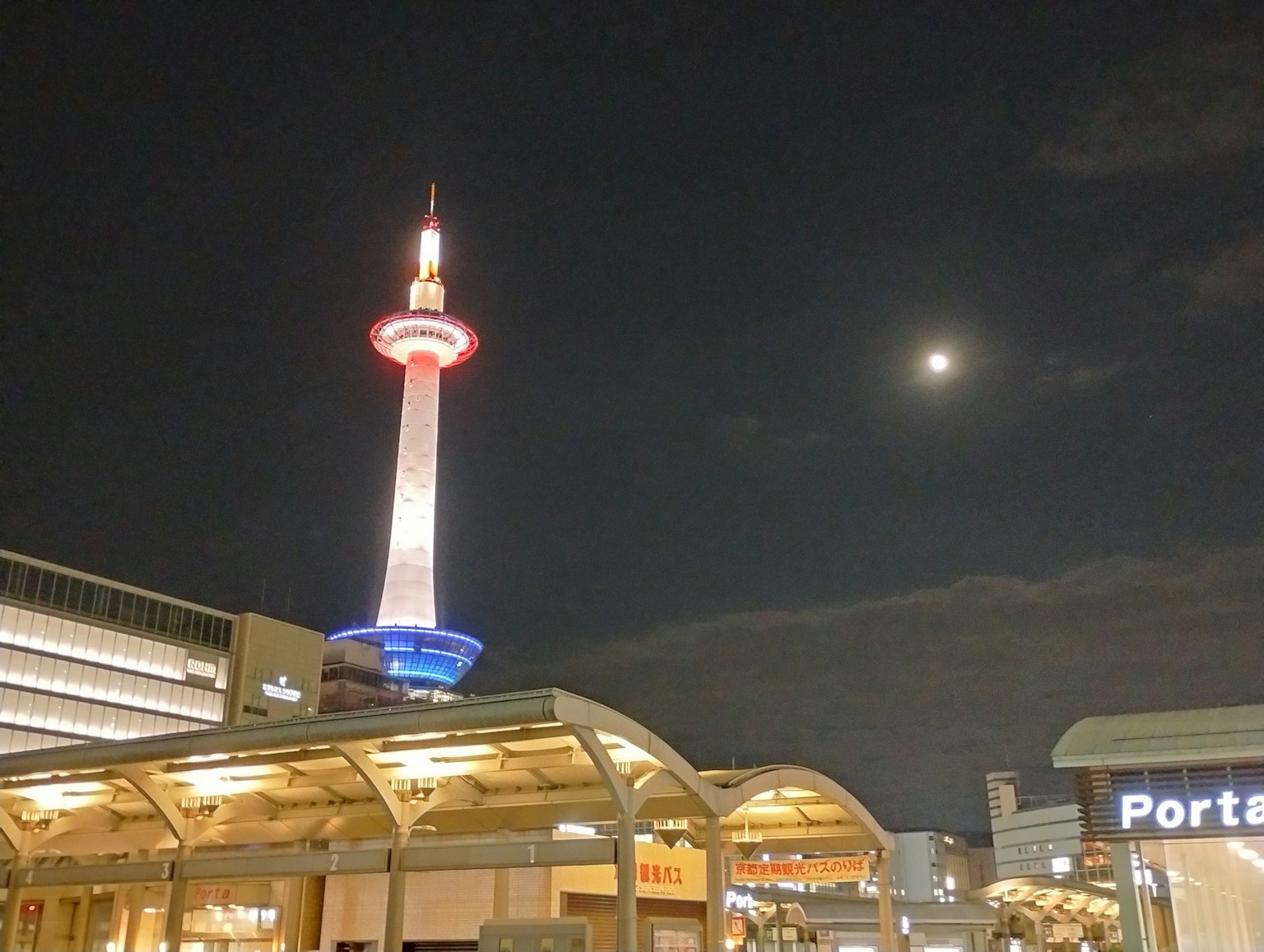 Kyoto Tower illuminated at night with a visible moon