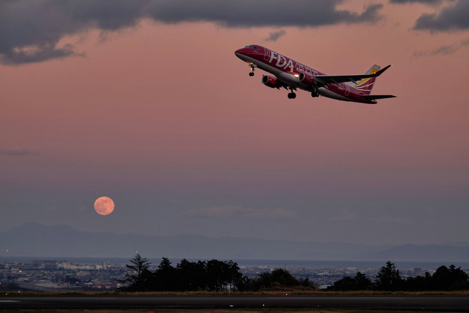 Avion décollant contre un ciel de coucher de soleil avec une pleine lune