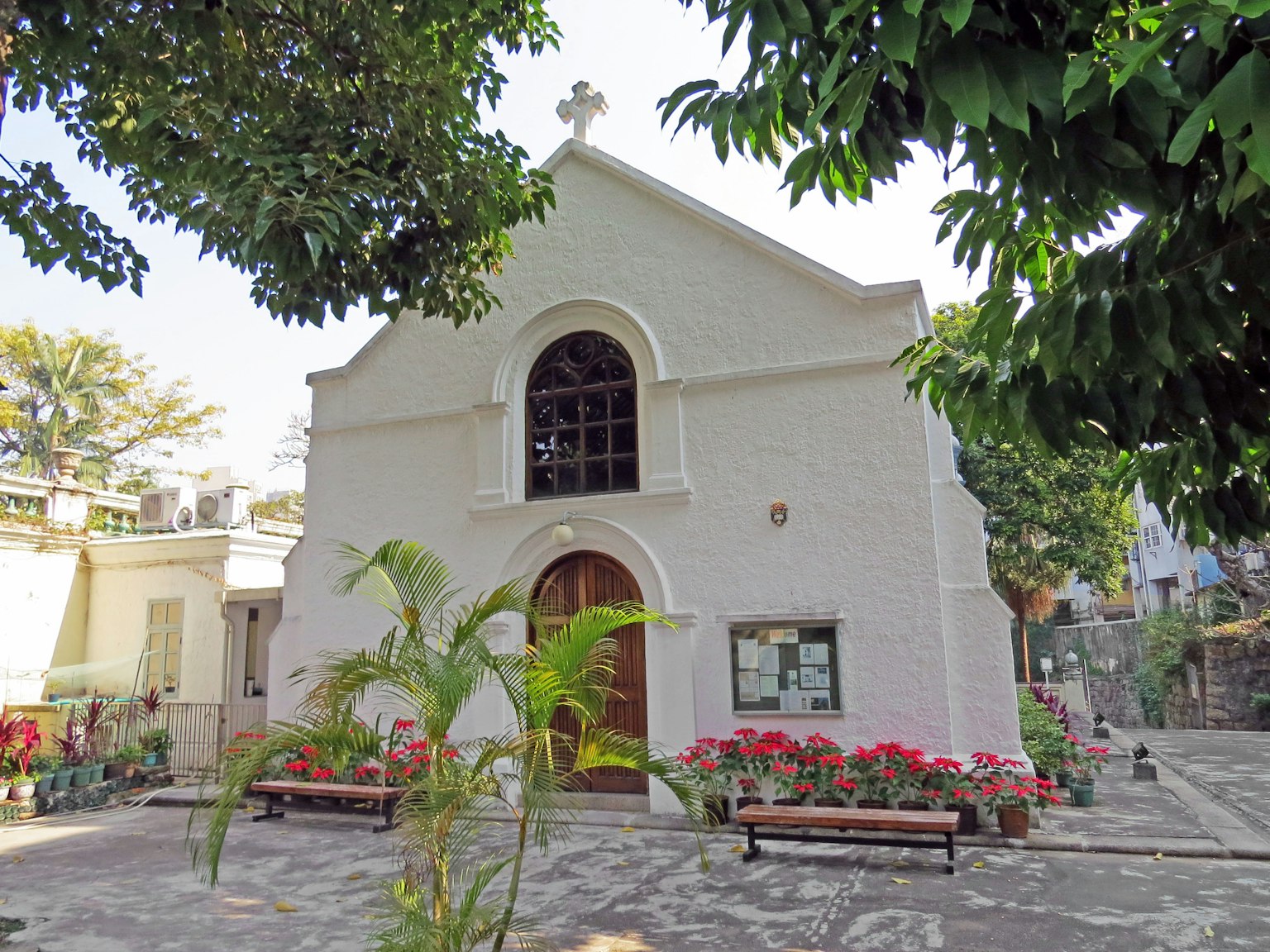 Weißes Kirchengebäude umgeben von grünen Bäumen und bunten Blumen