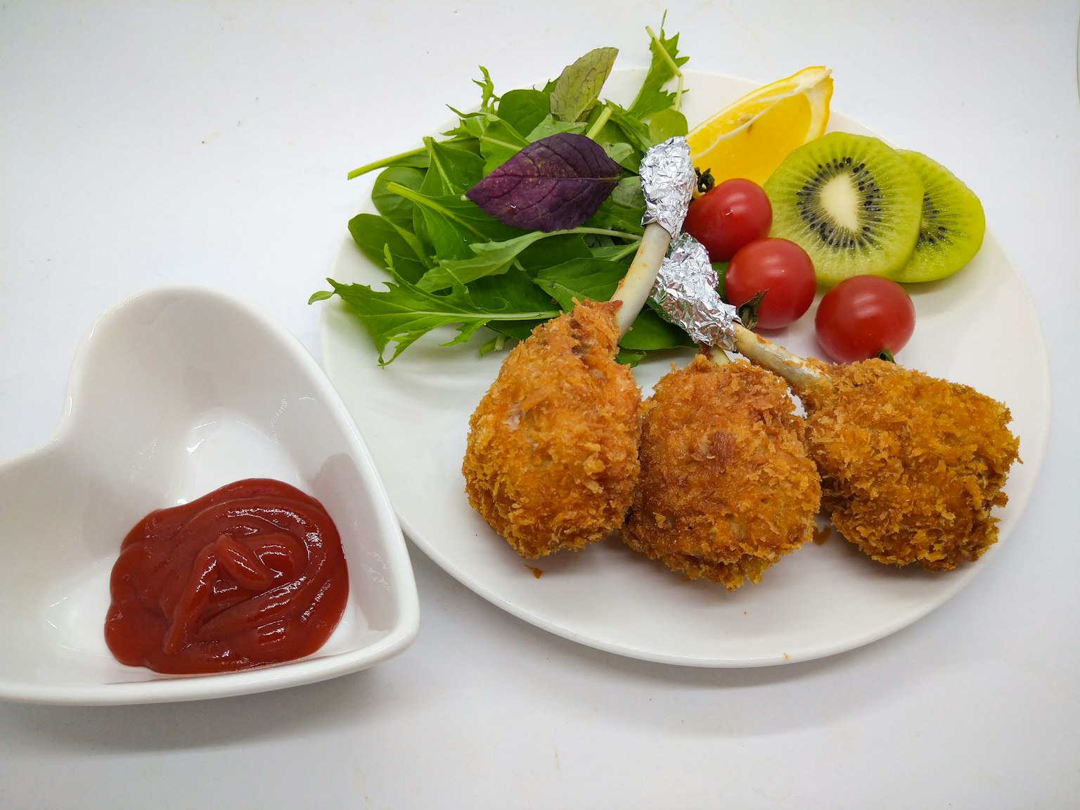Plato de pollo frito con ensalada colorida y frutas como kiwi y tomates cherry