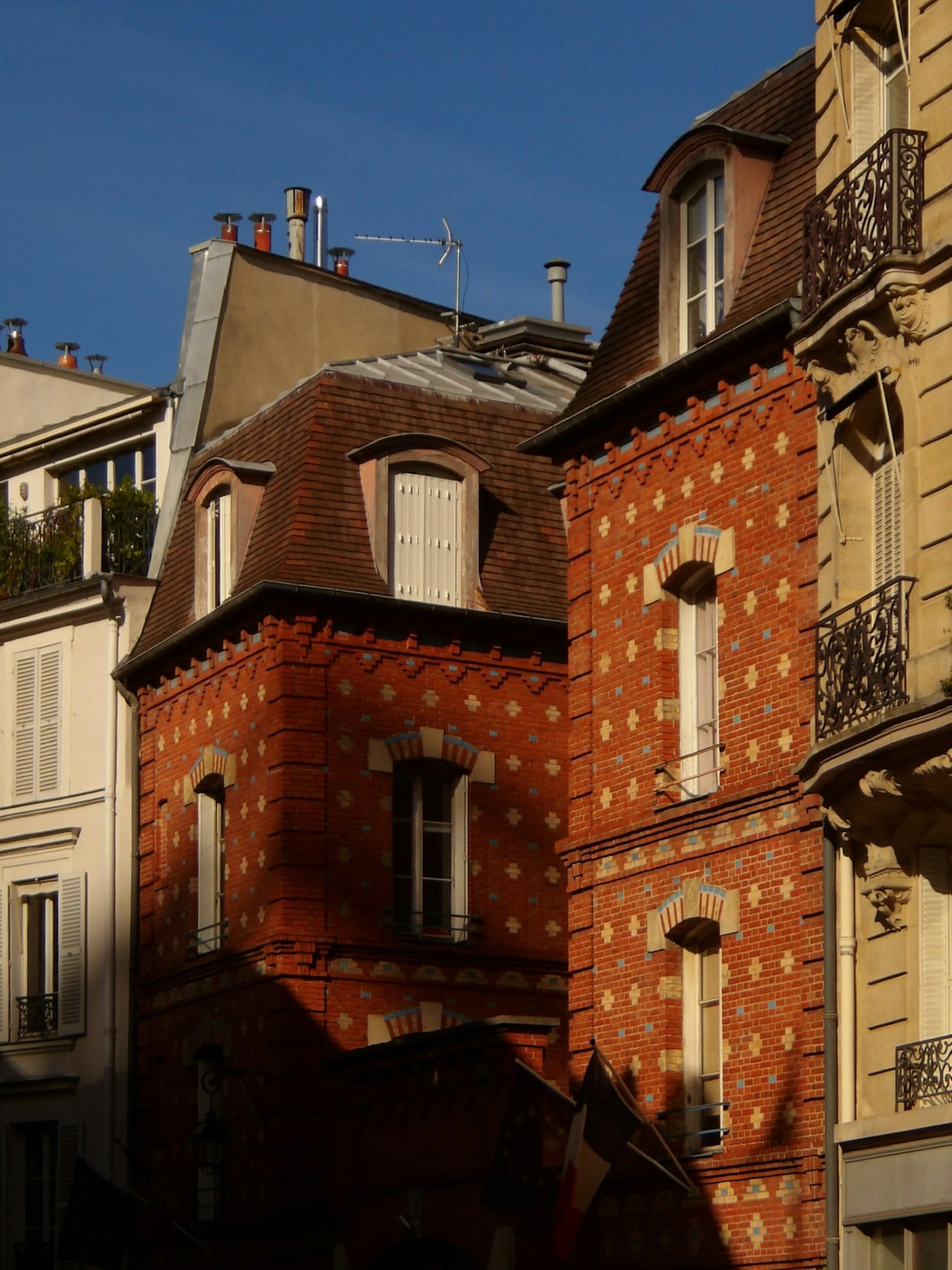 Bâtiments en briques rouges à Paris avec des caractéristiques architecturales distinctives sous un ciel bleu lumineux