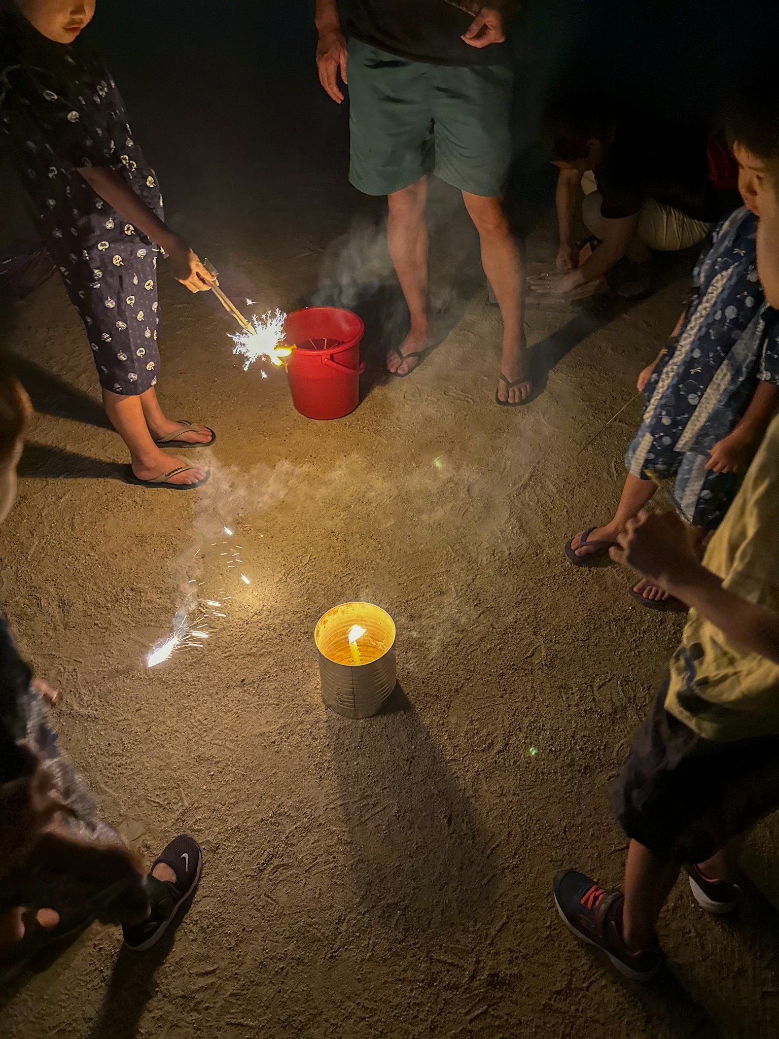 Children holding sparklers in a night scene playing around a large candle