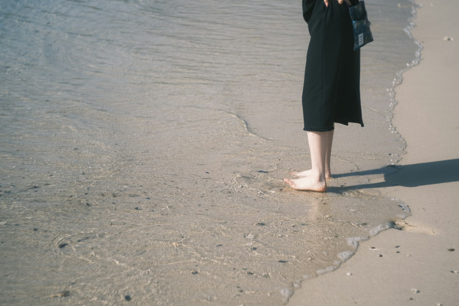 Persona in piedi sulla spiaggia con i piedi nell'acqua