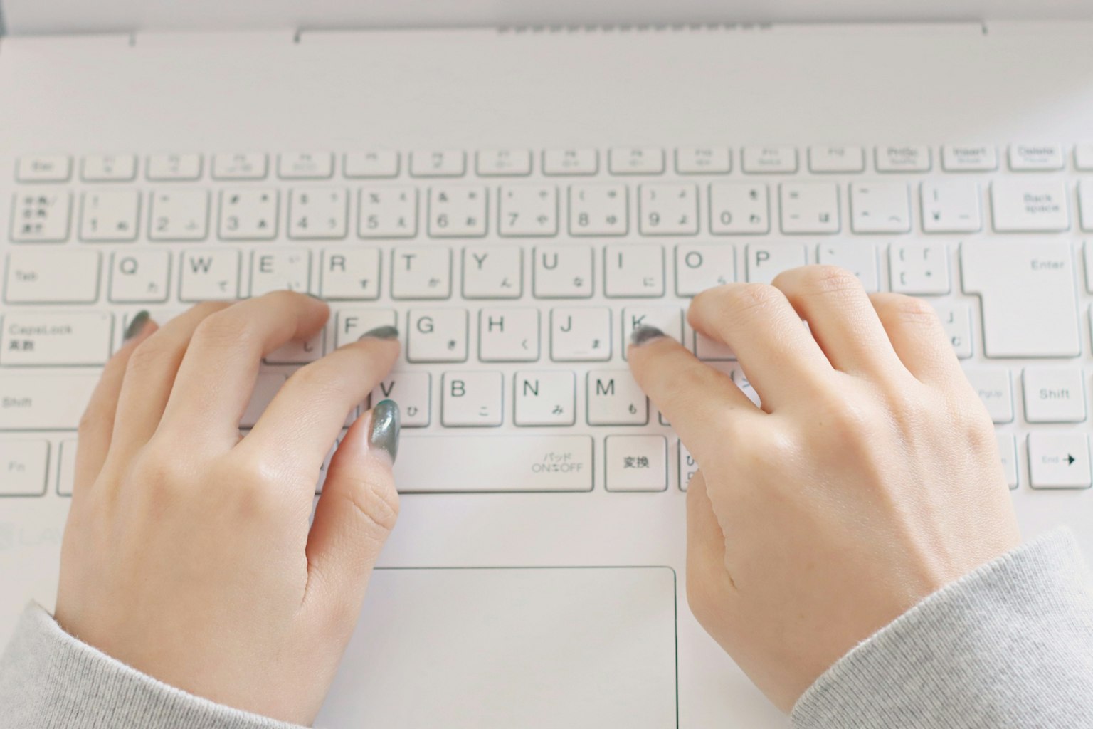 Manos escribiendo en un teclado de laptop blanco