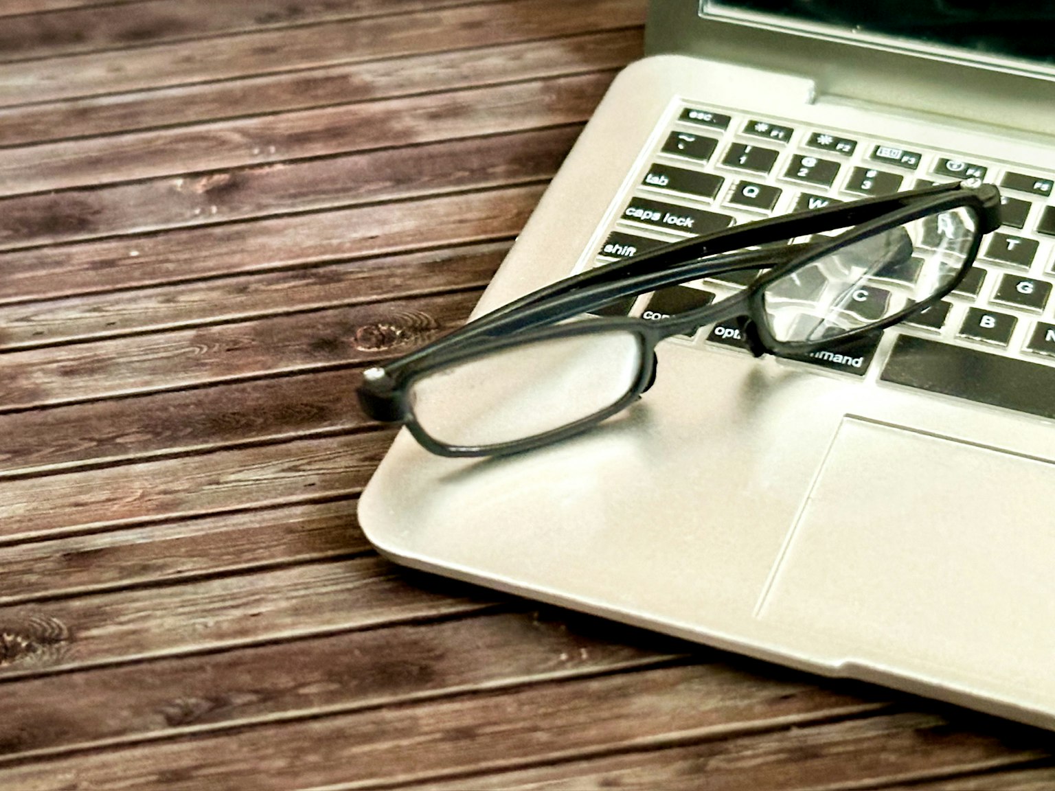 Laptop dengan kacamata di atas meja kayu