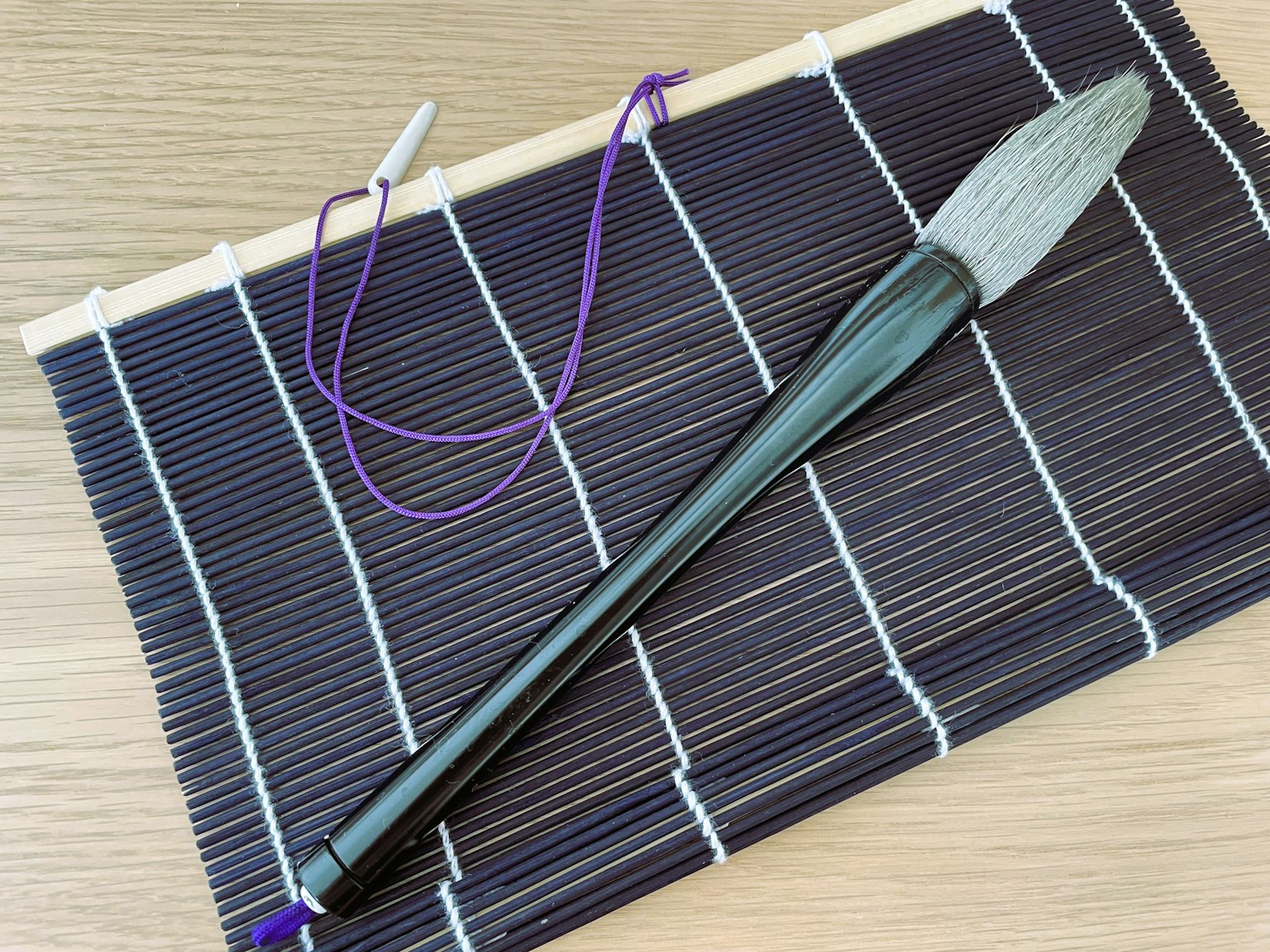 Schwarzer Pinsel mit lila Schnur auf einer Matte
