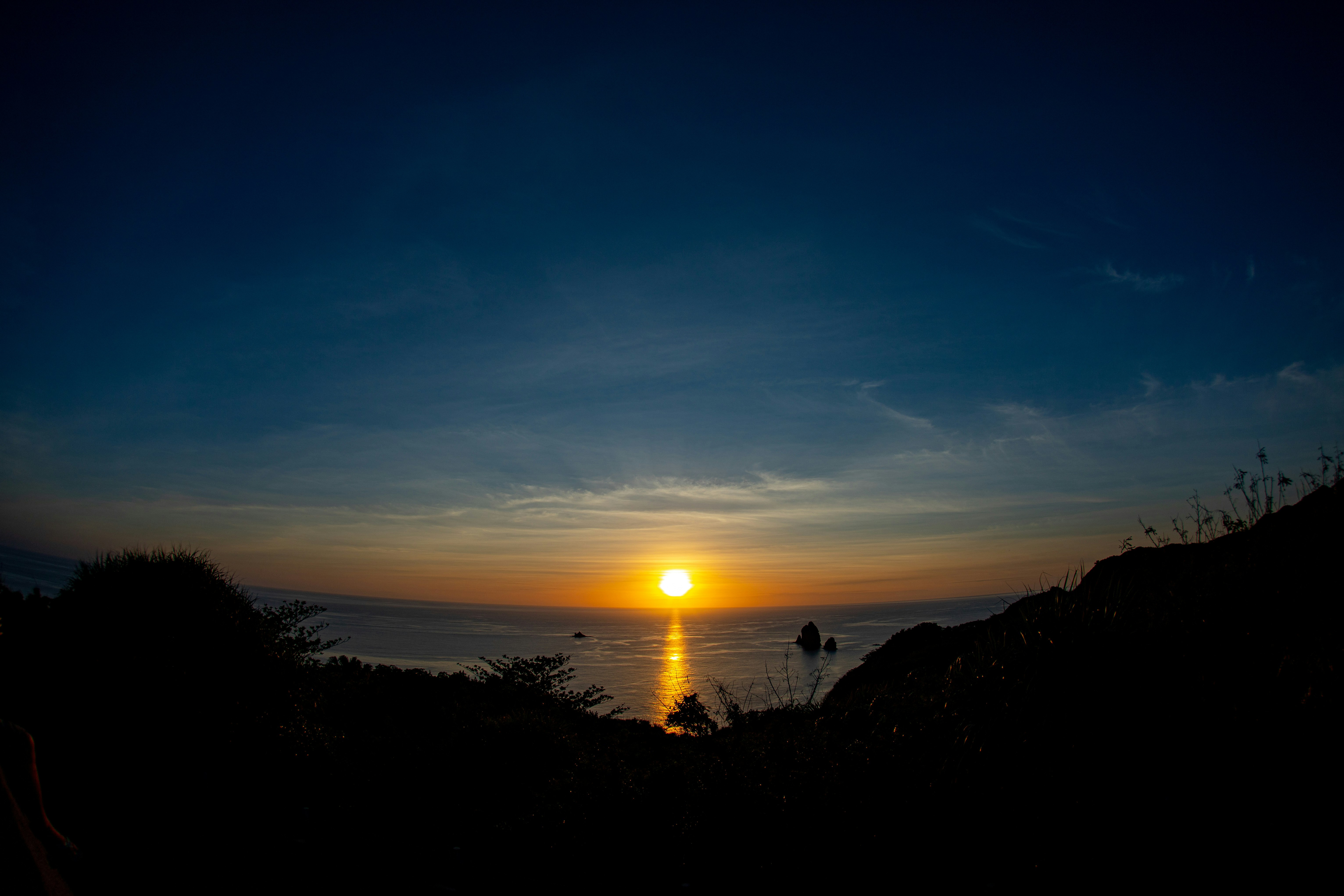 夕日が海に沈む山稜の向こうの海岸風景