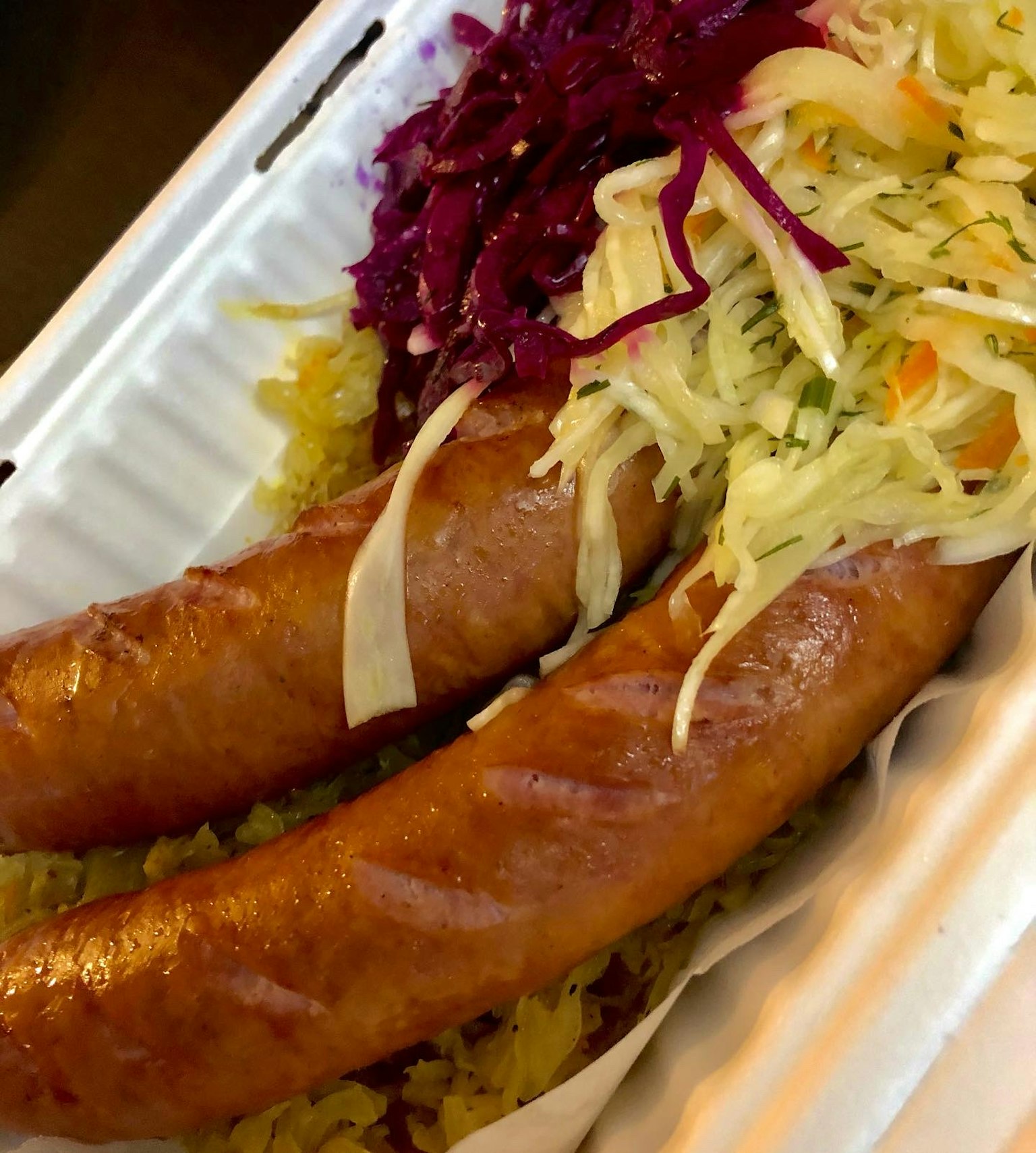 Piring dengan dua sosis disajikan dengan kol berwarna dan salad