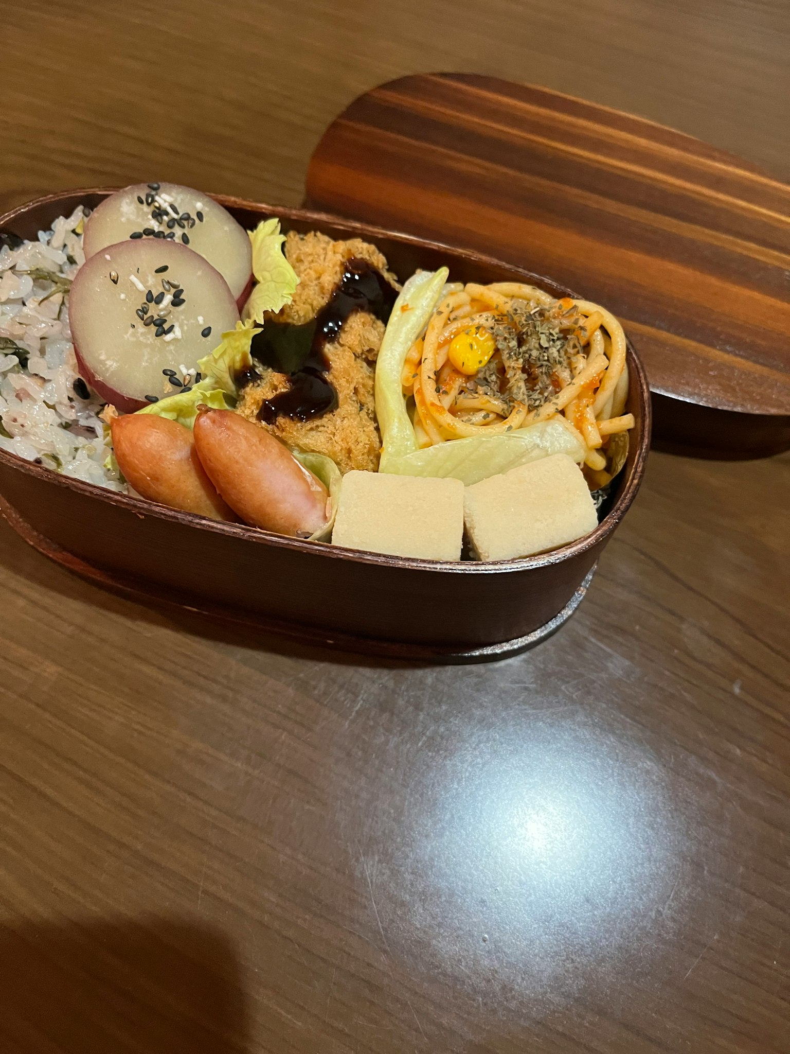 Boîte à bento avec du riz, du poulet frit, des spaghetti, une omelette, des légumes et des boulettes de dessert