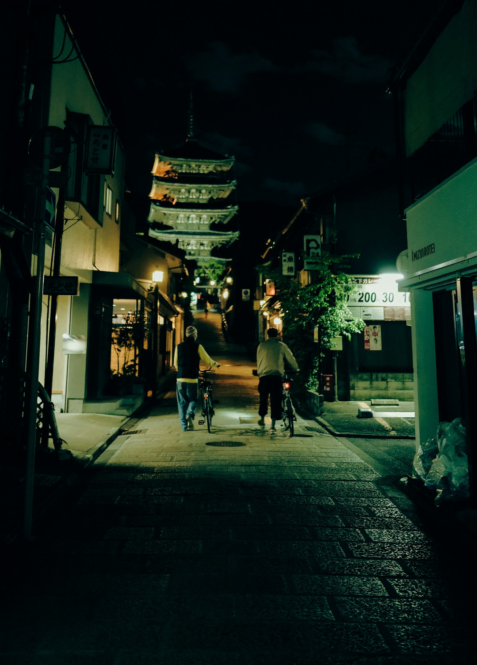 兩個人騎自行車經過夜晚安靜的街道，掛著燈籠