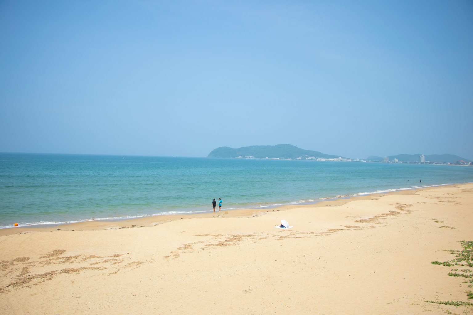 Người đi bộ trên bãi biển cát với biển xanh và hòn đảo ở xa